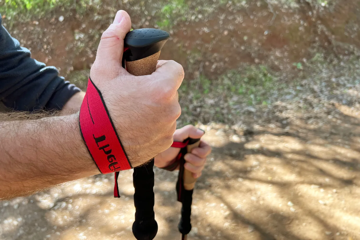 Hands holding trekking poles with straps at an outdoor setting