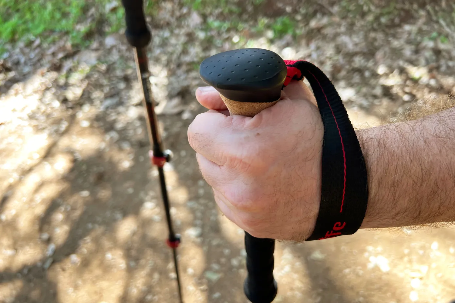 Hand holding the handle of a trekking pole with a wrist strap attached seen on an outdoor trail