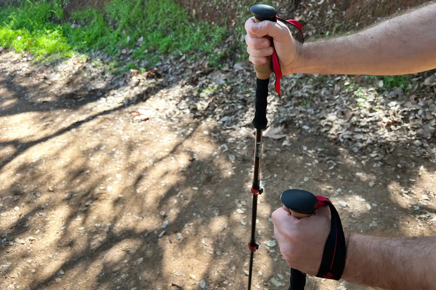 Closeup of hands gripping hiking poles on a dirt trail outdoors with foliage in the background