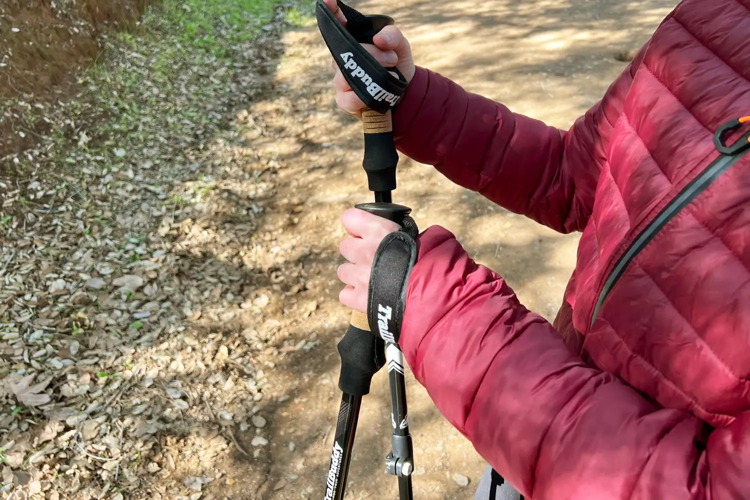 Person holding trekking poles on a dirt path wearing a red jacket