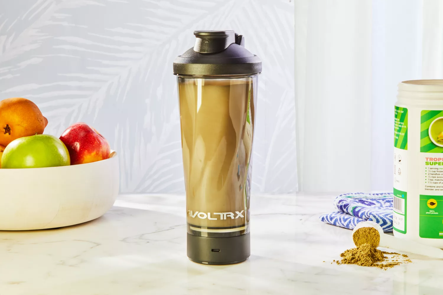 VOLTRX Premium Electric Protein Shaker Bottle displayed on counter with powder and fruit