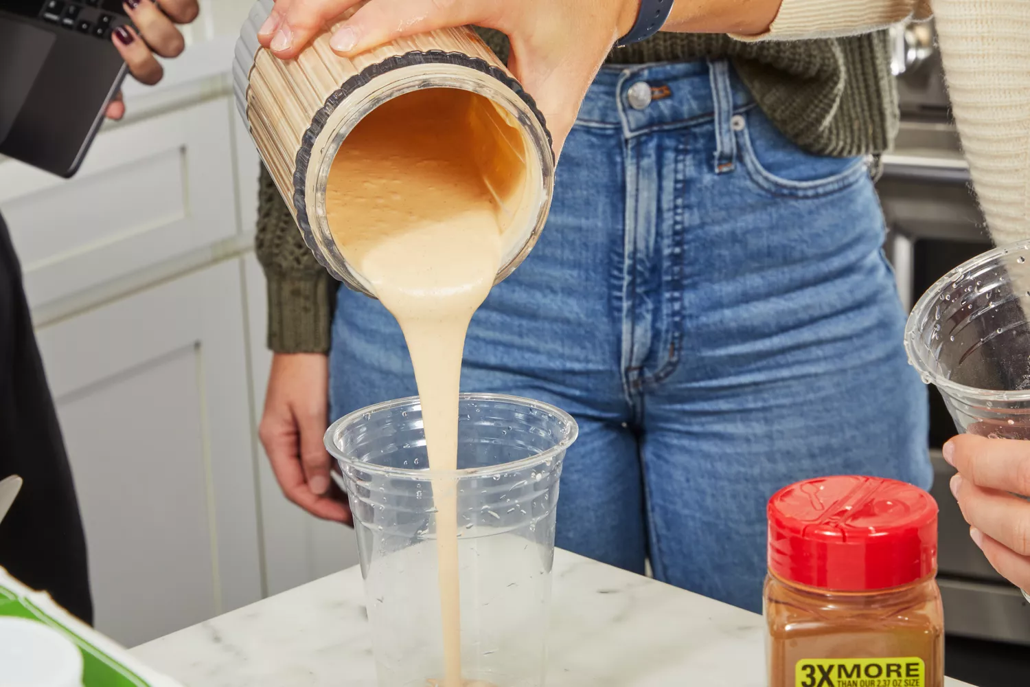 Person pouring smoothie into plastic cup