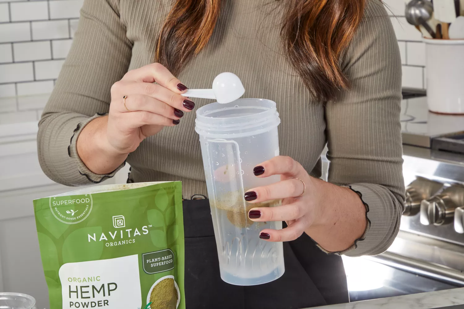 A hand adds a scoop of Navitas Organics Hemp Powder to a protein shaker