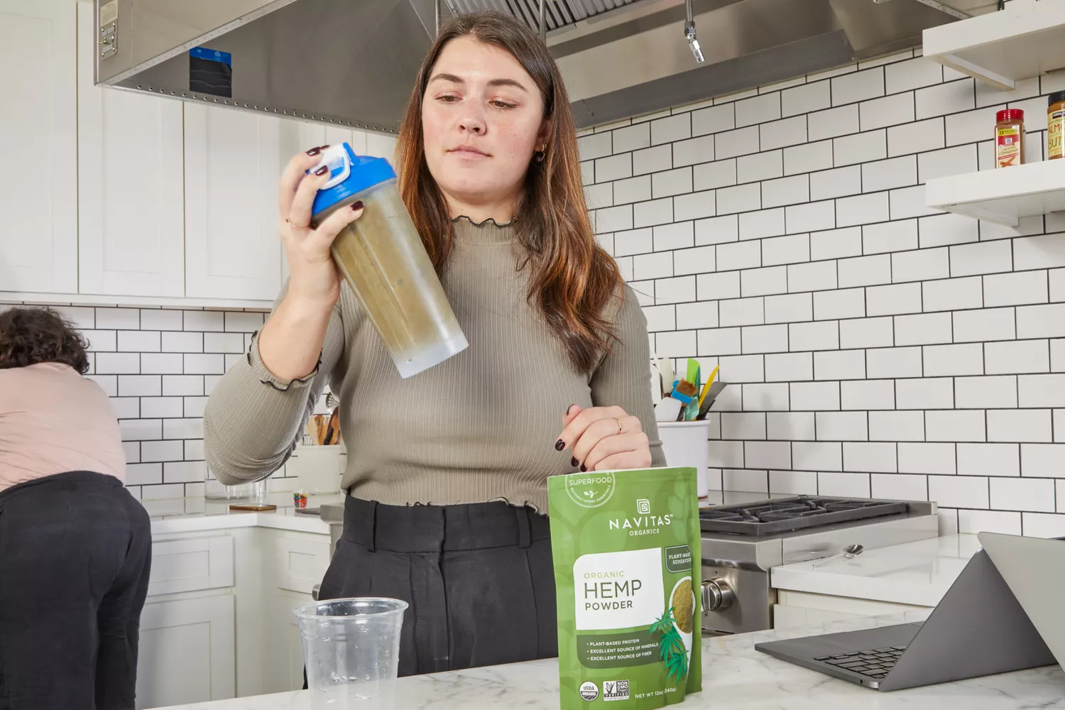 A person uses a protein shaker with Navitas Organics Hemp Powder on marble counter