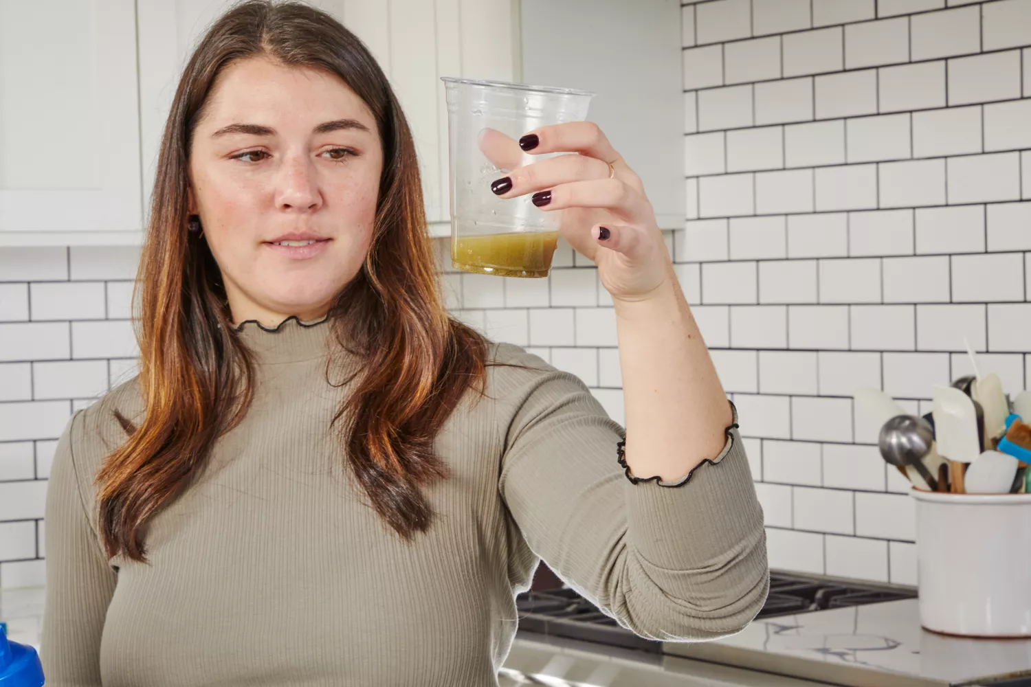 A person holding a plastic cup full of liquid in kitchen