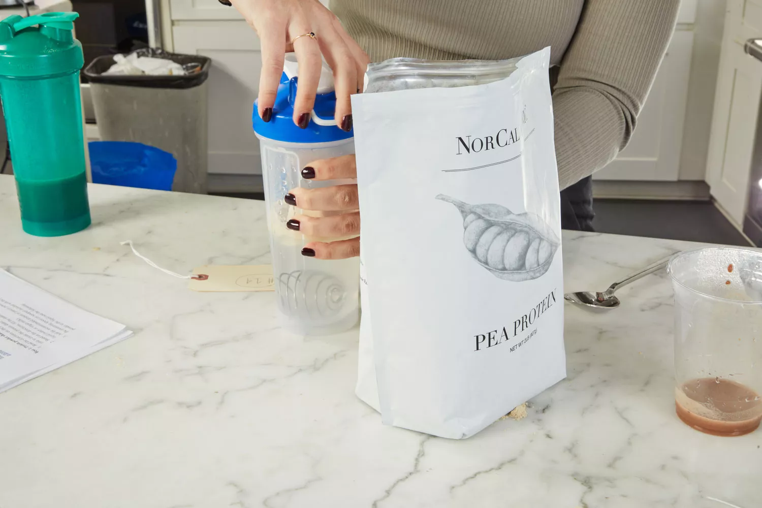 NorCal Organic Premium Pea Protein next to two hands holding a blender bottle on a marble counter
