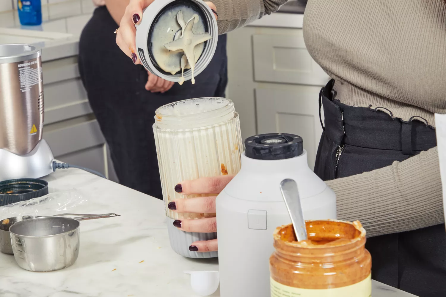 A hand removes a blender base from the cup on a marble counter