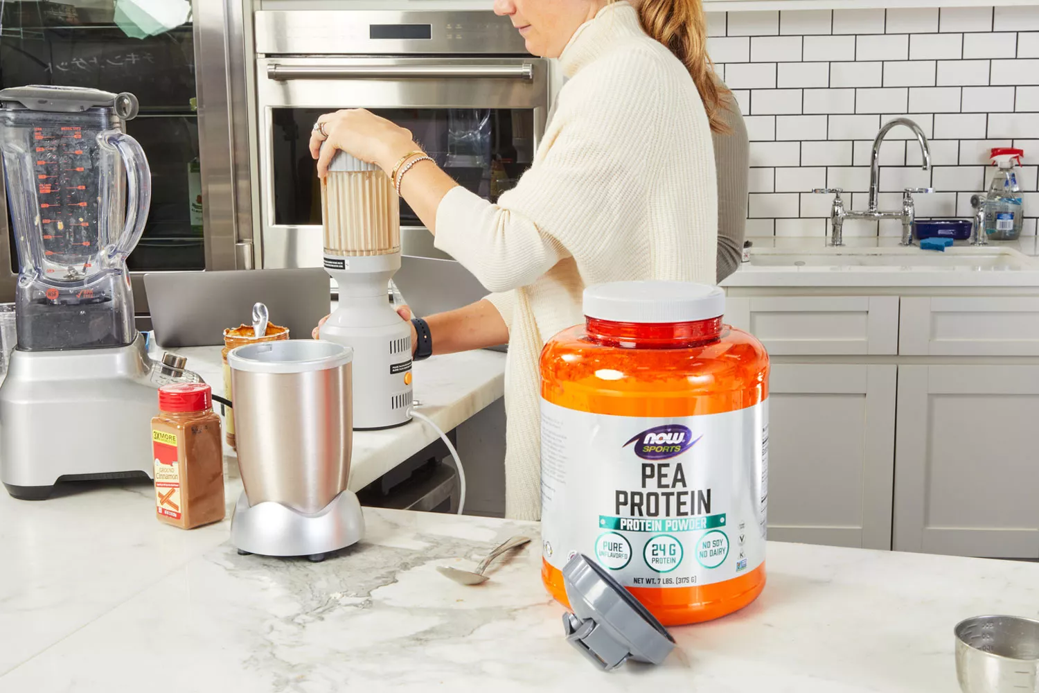 NOW Sports Pea Protein on marble counter with person making smoothie in background