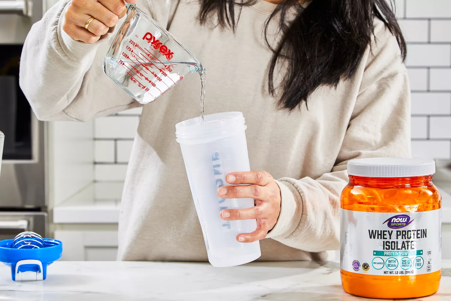 A person pours water into a blender bottle of NOW Sports Nutrition Whey Protein Isolate