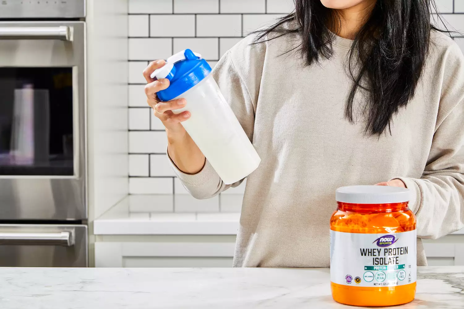 A person shakes up a blender bottle of NOW Sports Nutrition Whey Protein Isolate