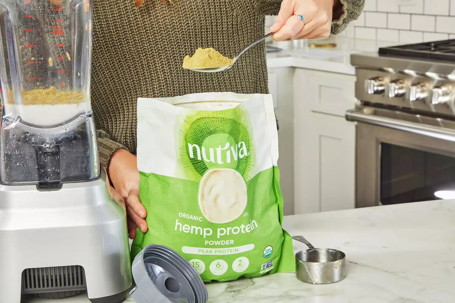 A hand scooping out Nutiva Hemp Seed Protein Powder next to a blender