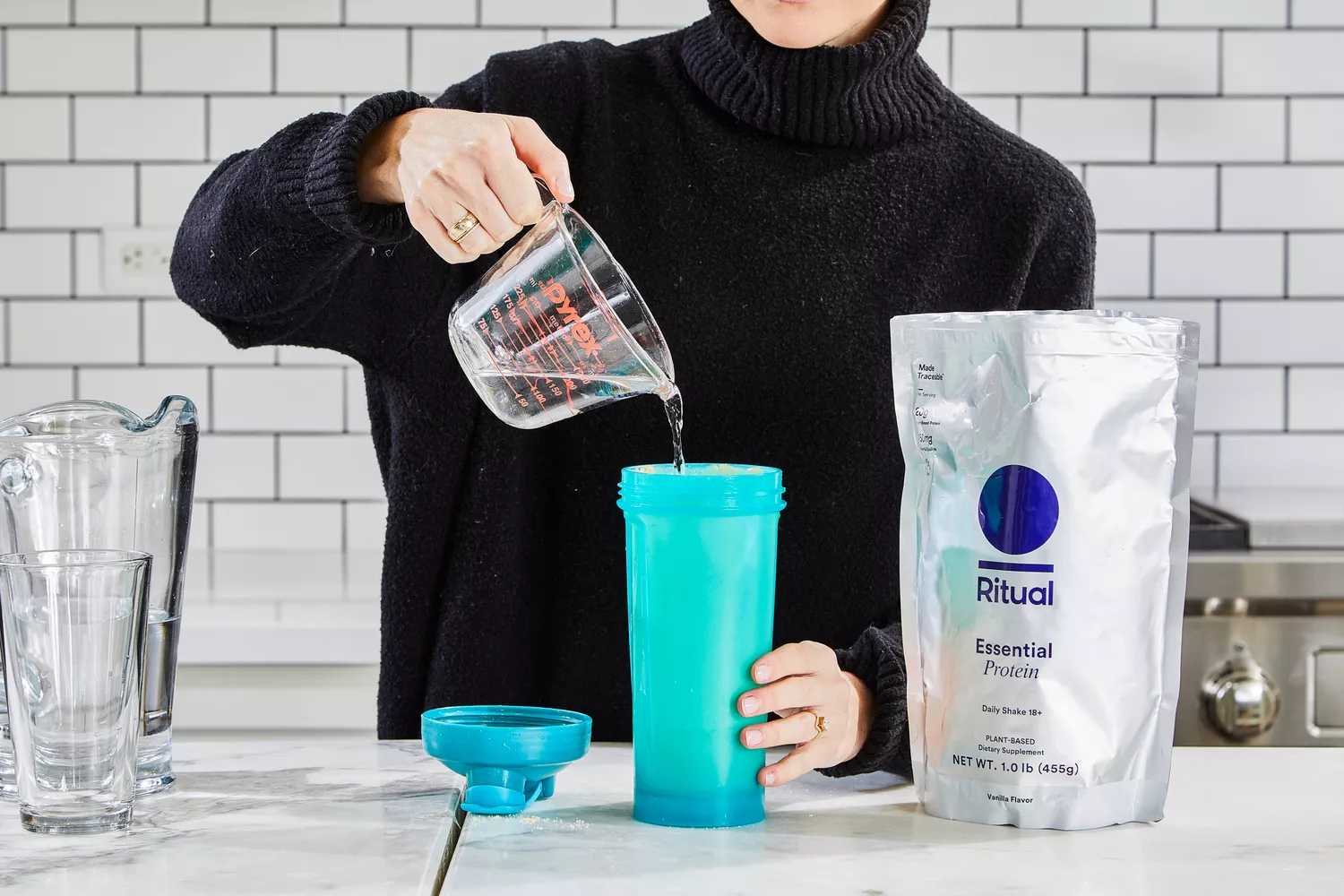 A glass of water is poured into Ritual Essential Protein Daily Shake Protein Powder