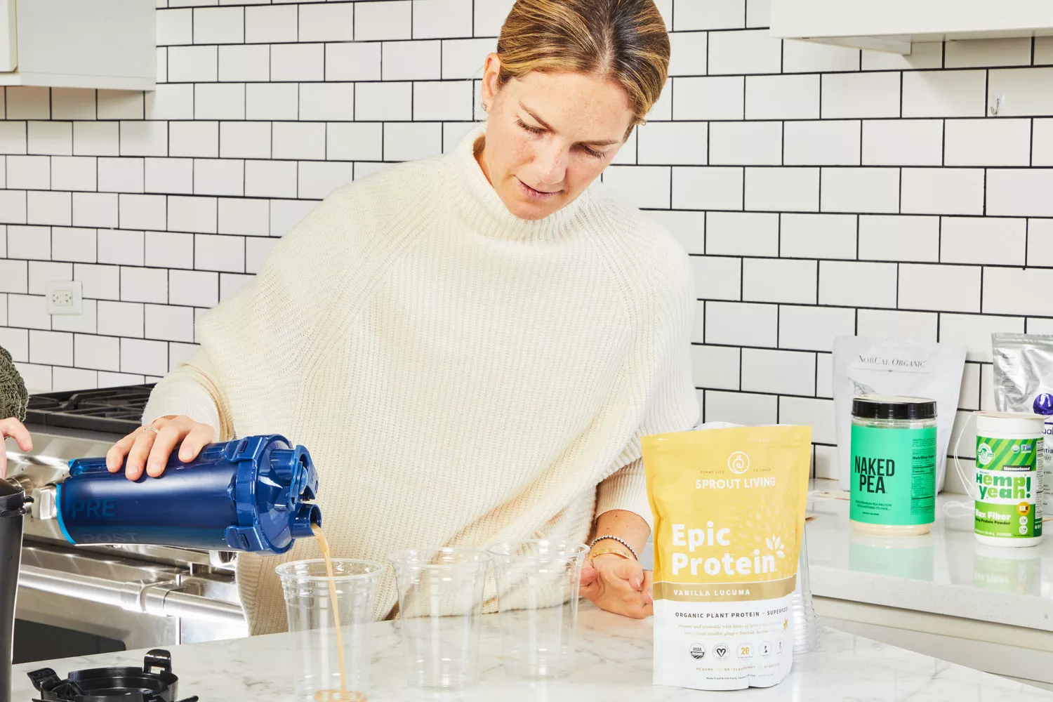 Person pouring liquid into plastic cups next to Sprout Living Epic Protein Vanilla Lucuma on marble counter