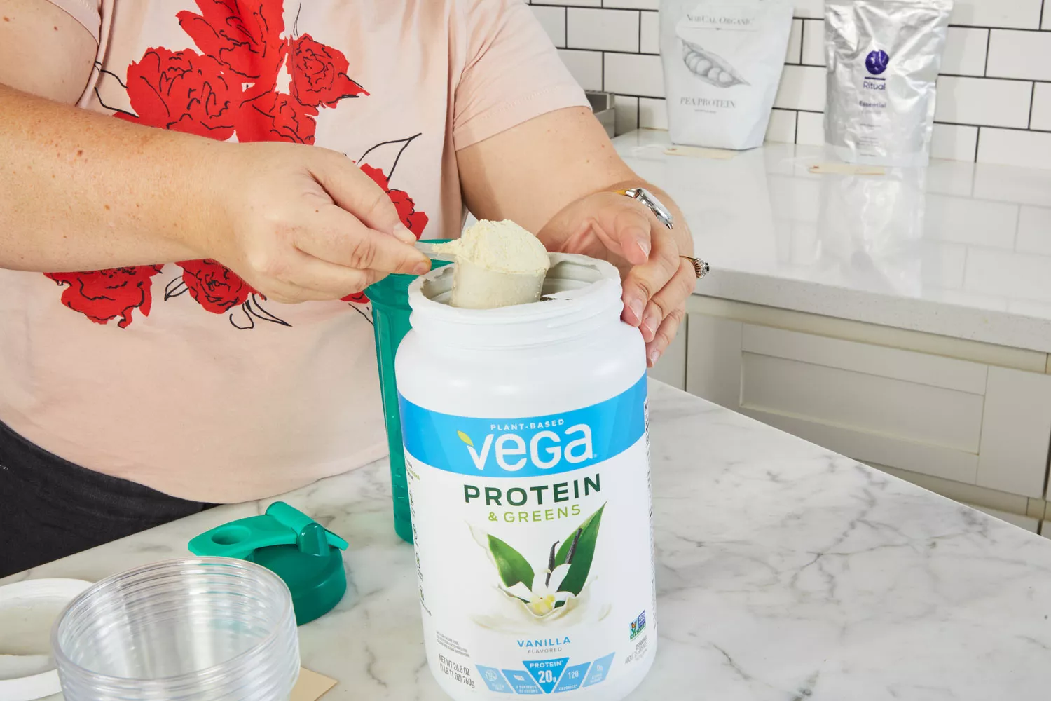A hand scooping out Vega Protein & Greens Plant-Based Protein Powder on marble counter
