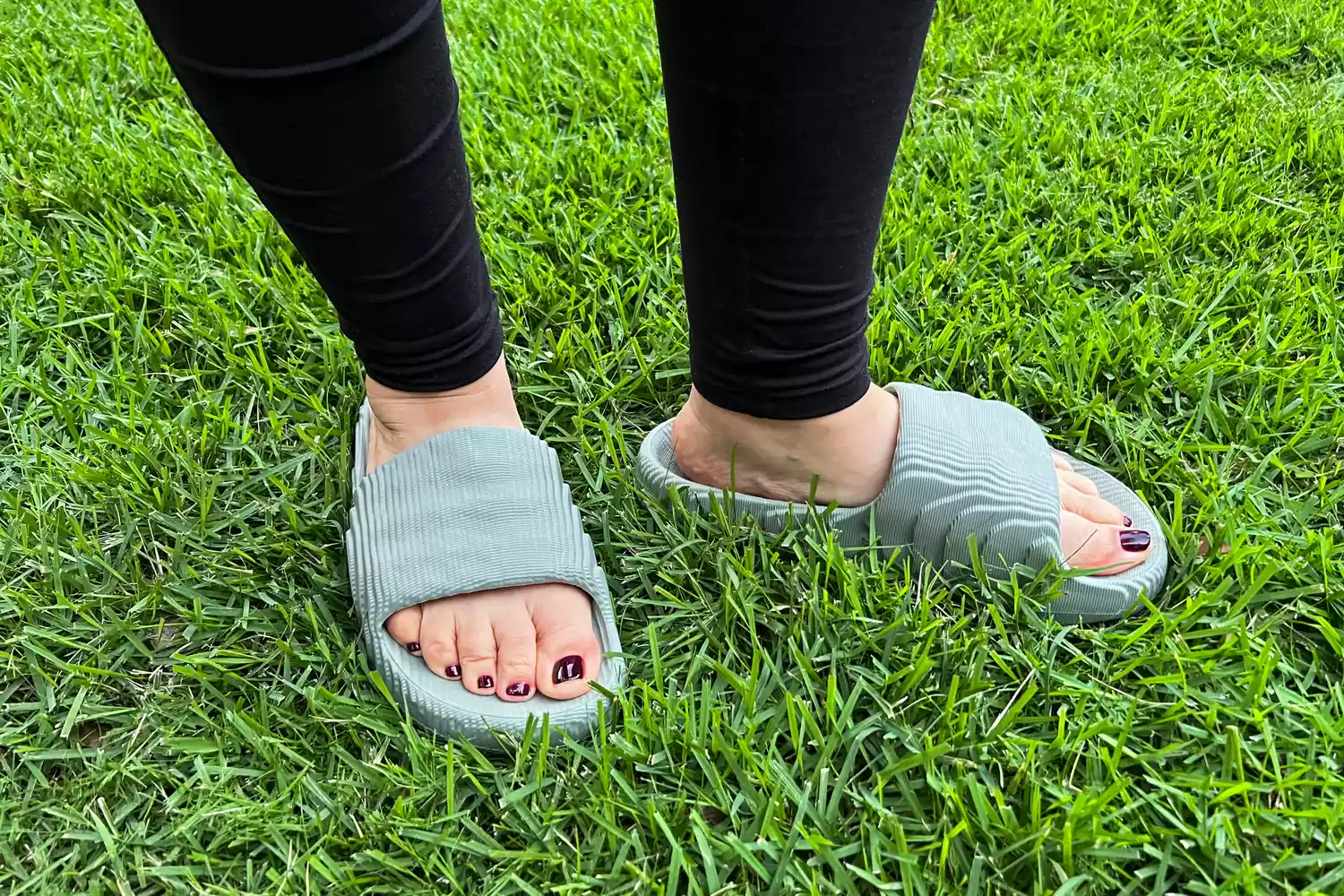 A person stands outside in grass while wearing the Adidas Adilette 22 Slides