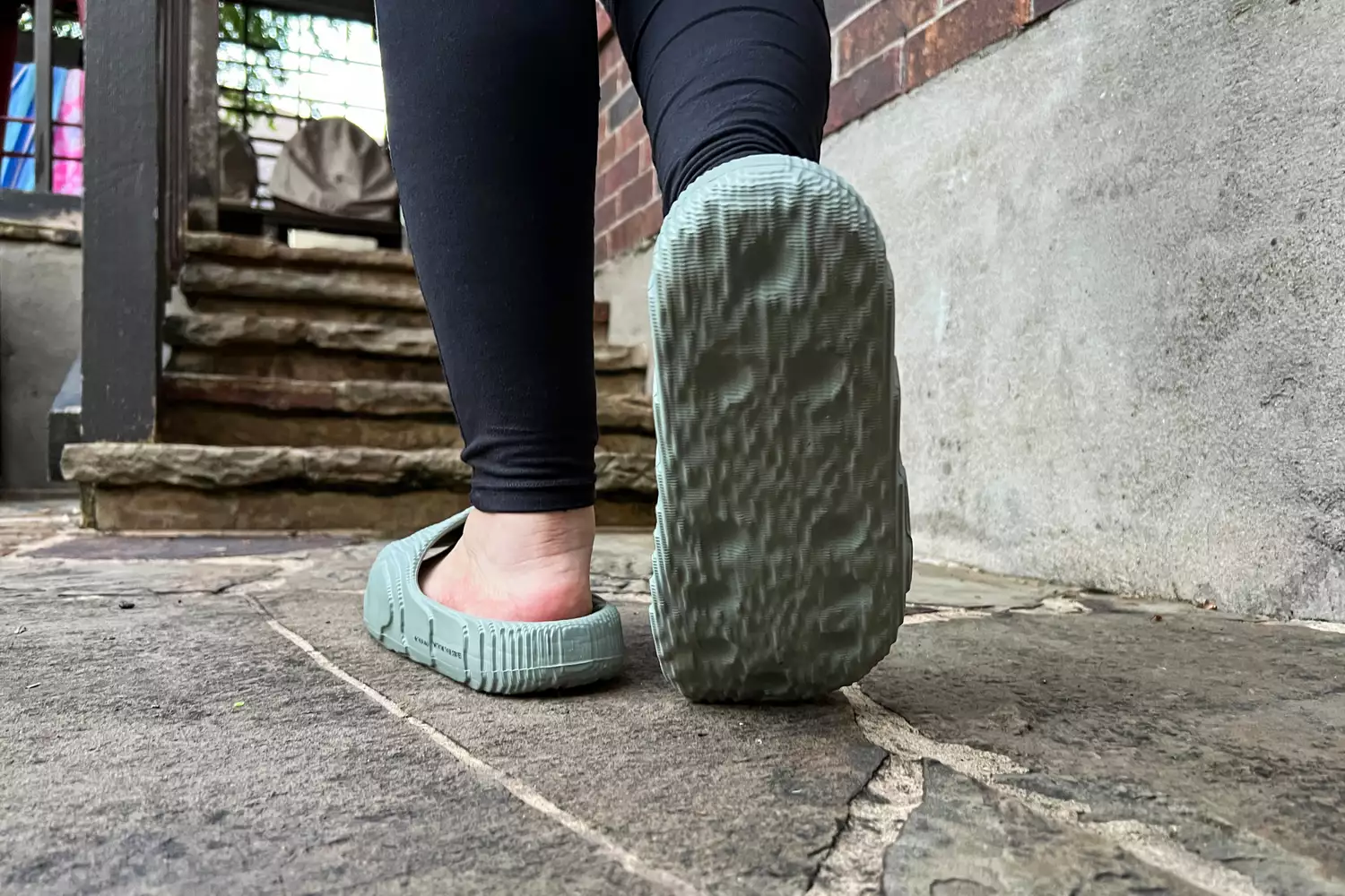 A person walks on stone while wearing the Adidas Adilette 22 Slides 