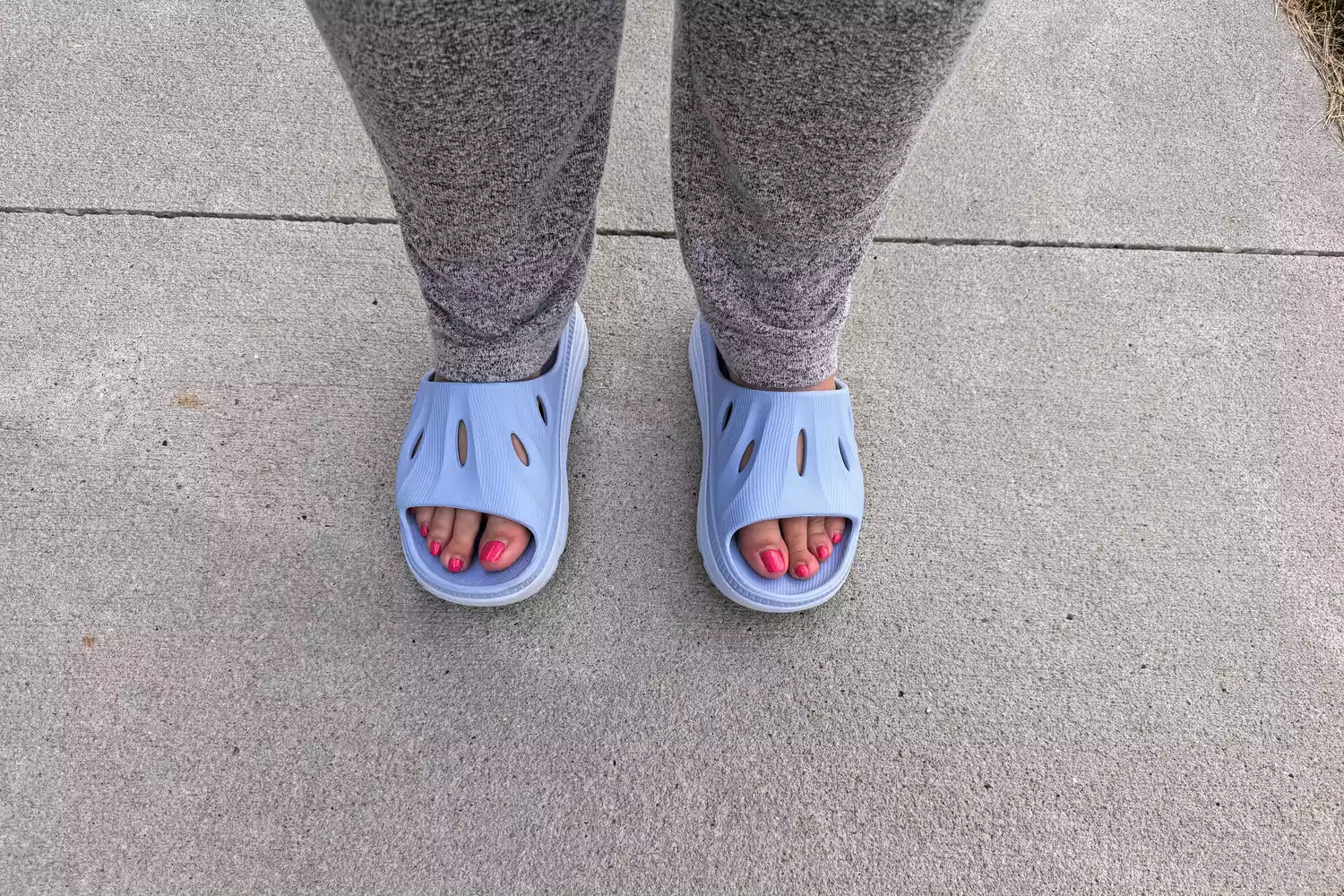 A person stands on concrete while wearing the ARISIC Recovery Slides