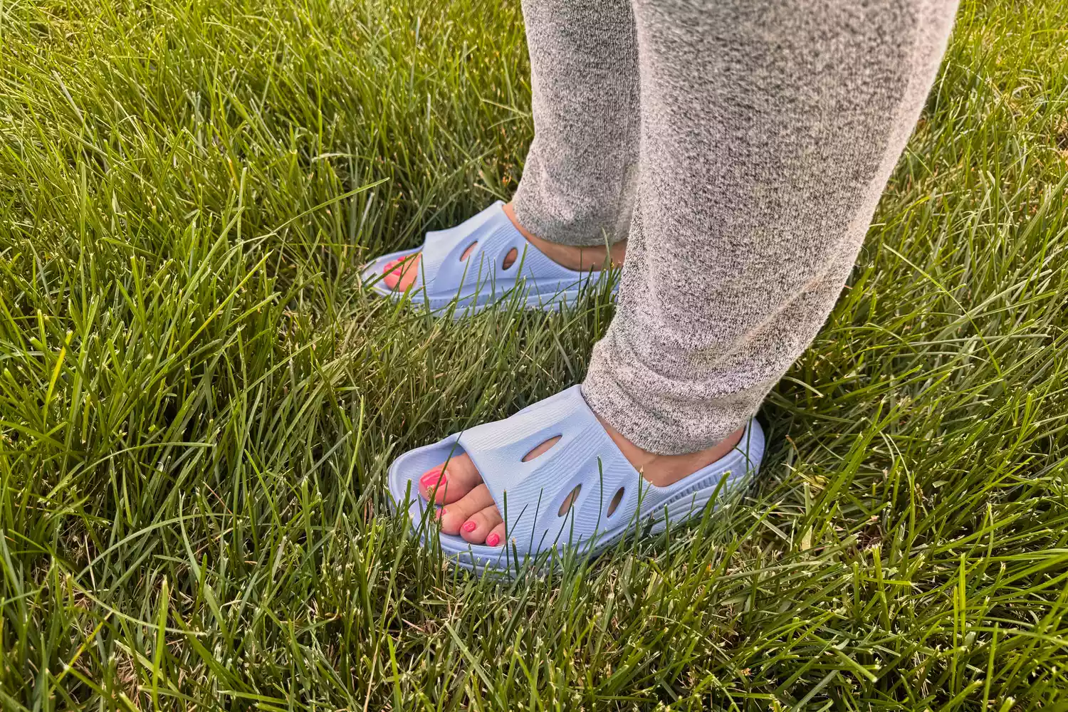 A person stands in grass while wearing the ARISIC Recovery Slides
