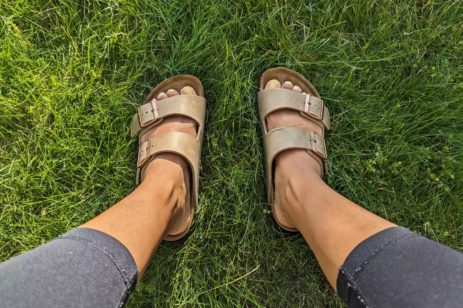 A person wears the Birkenstock Women's Arizona Soft Footbed Sandals in grass