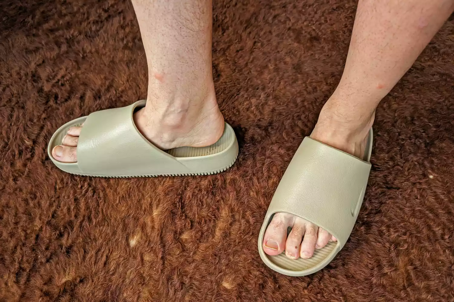 A person stands on a carpet while wearing the Nike Calm Men's Slides