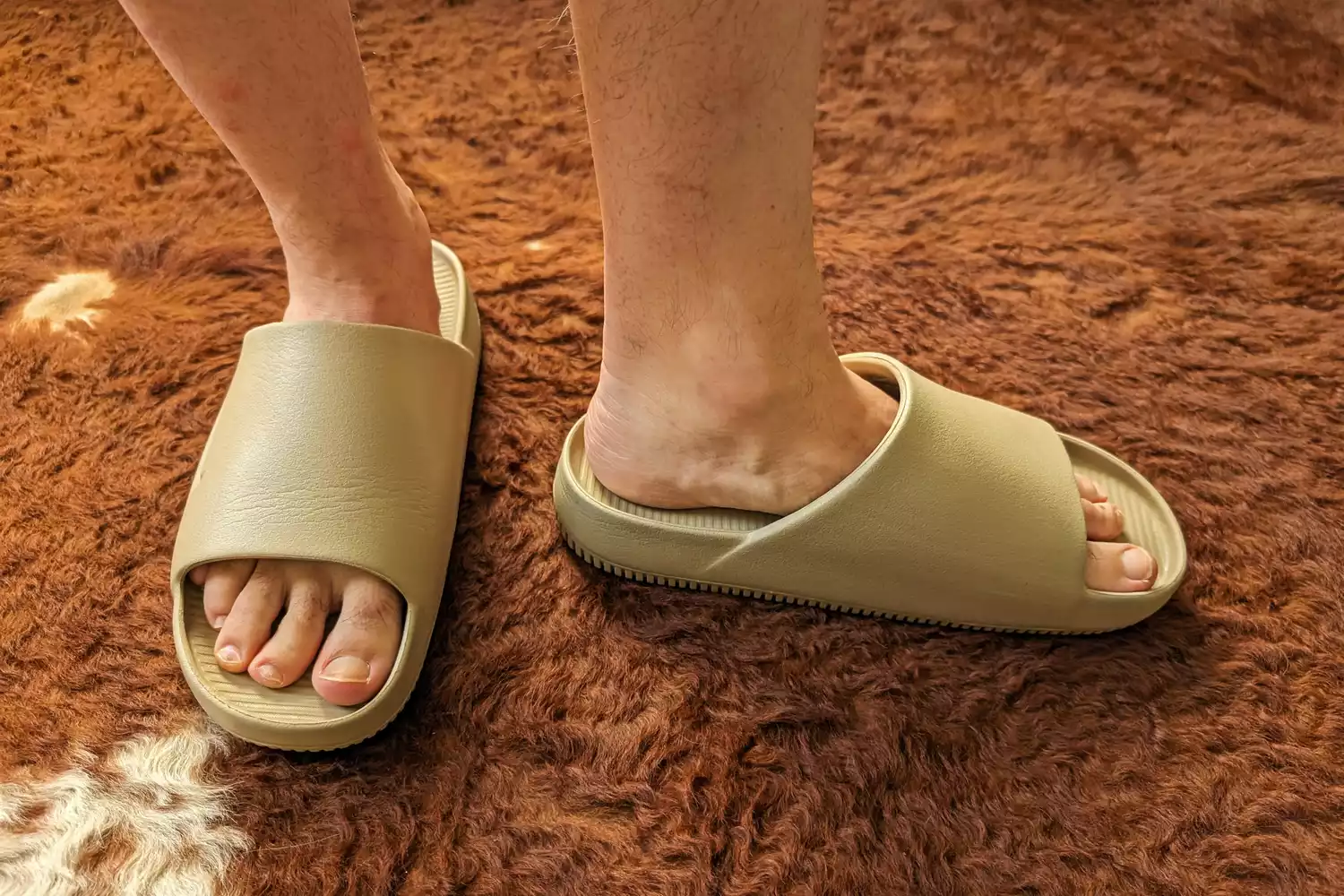 A person stands on carpet wearing the Nike Calm Men's Slides