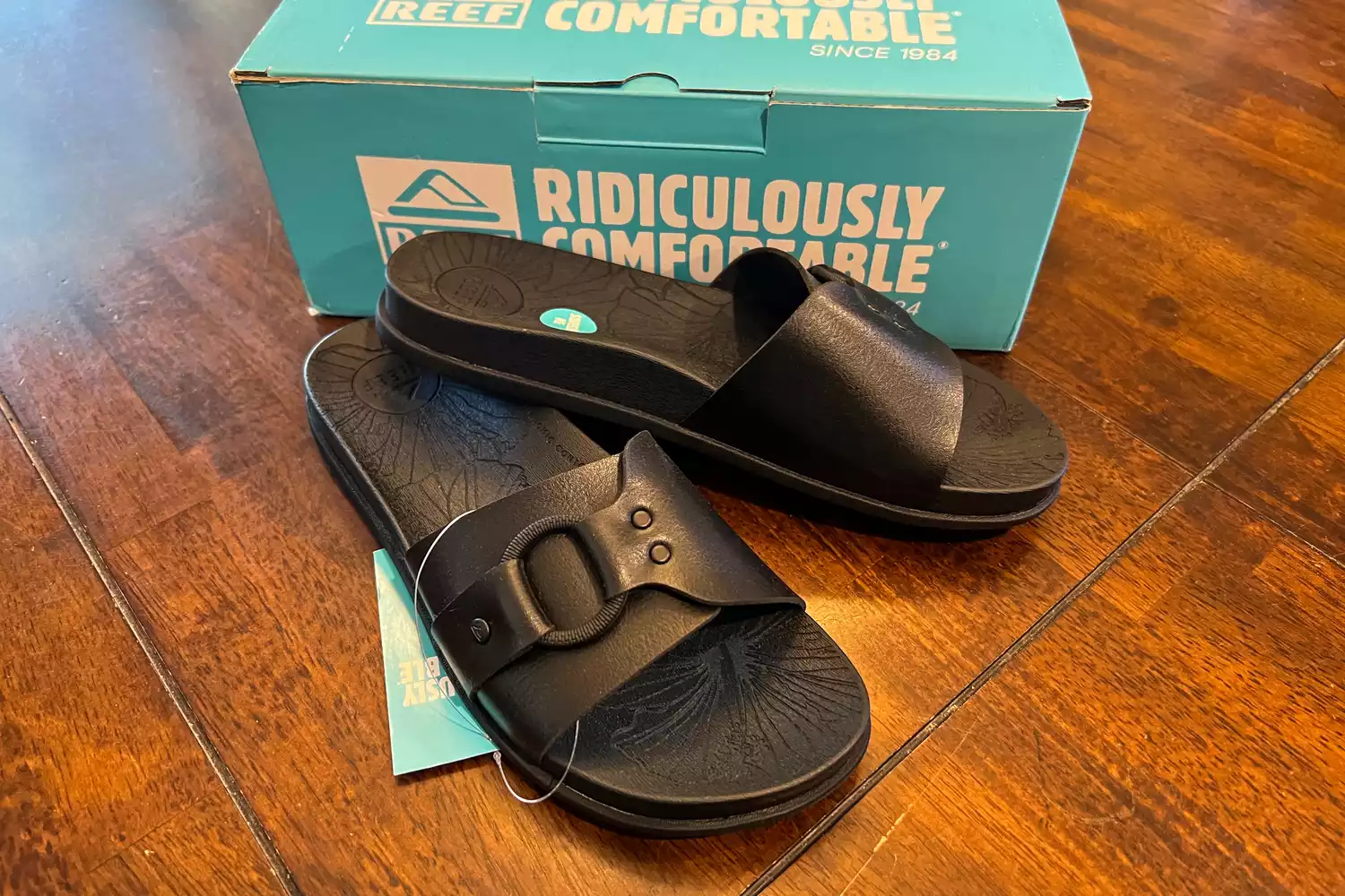 The Reef Women's Cushion Soho Cruz Sandals with the tags on in front of their box