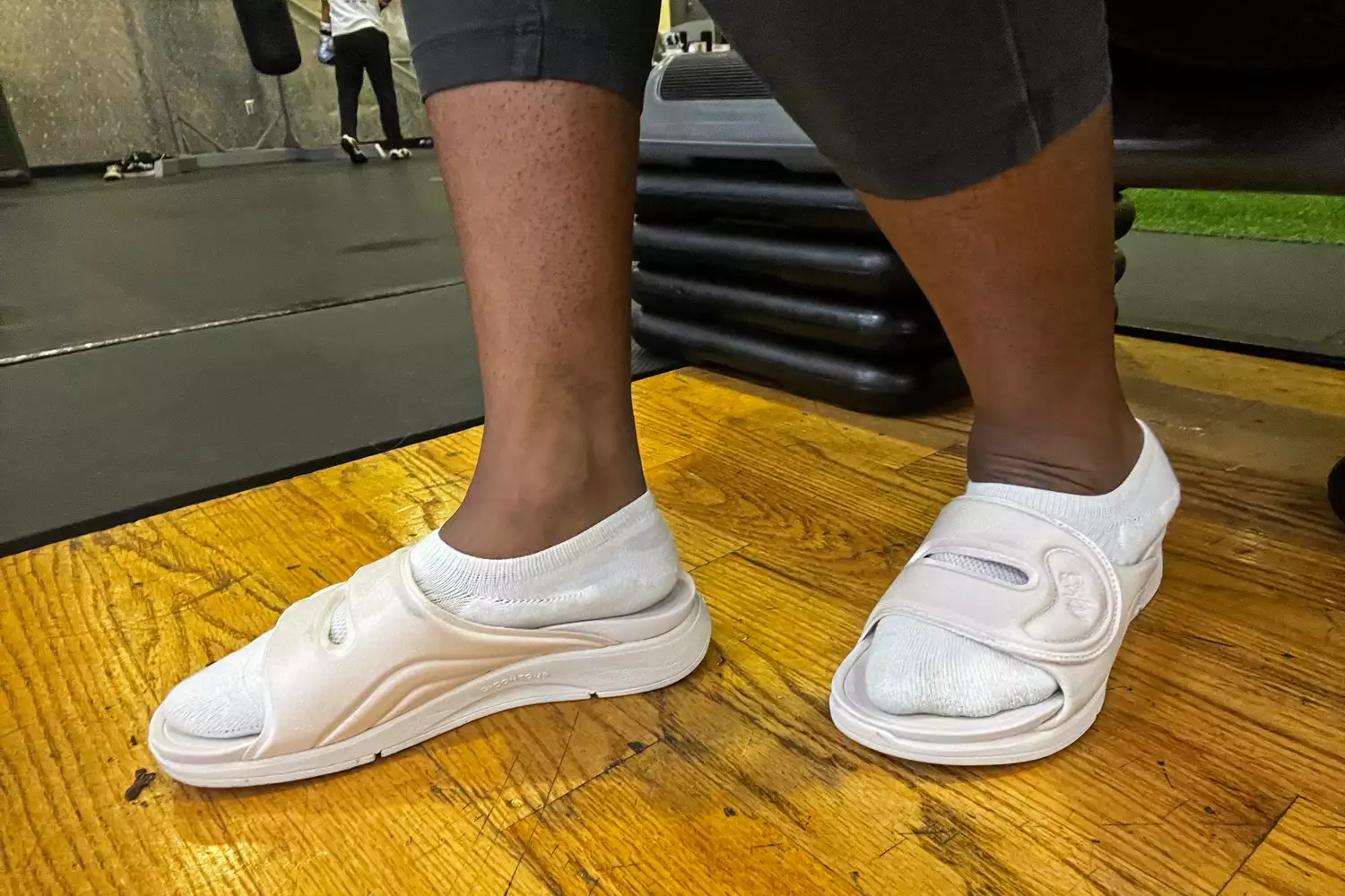 A person walks on a wood floor while wearing the Ryka Women's Tao Recovery Slide Sandals