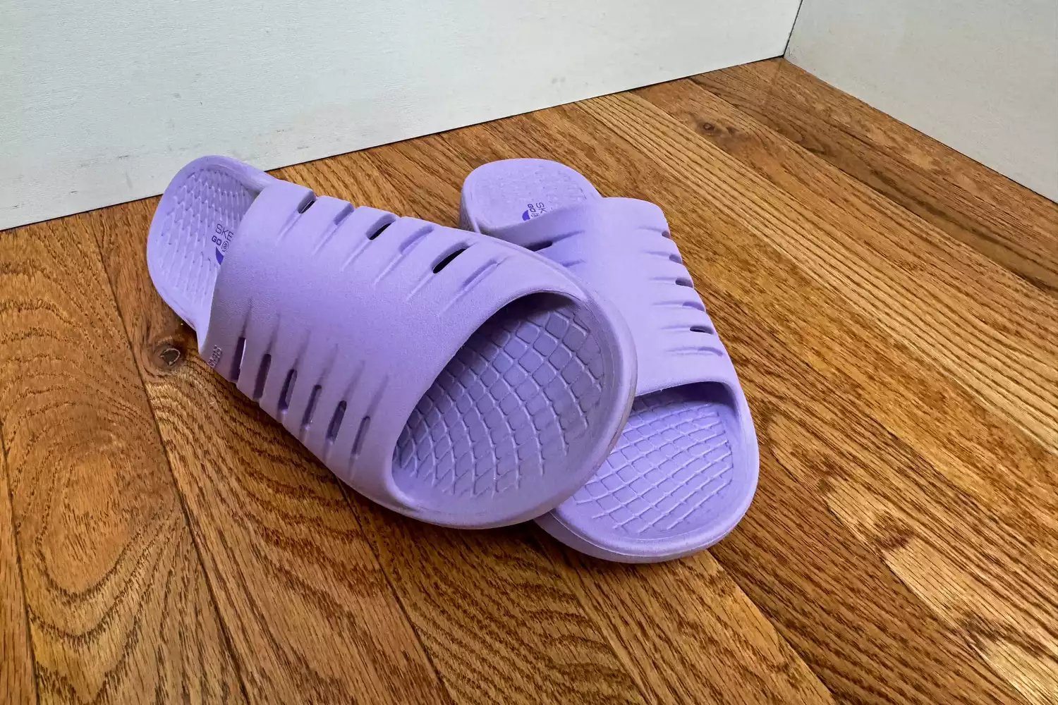 A front view of a pair of Skechers Women's GO RECOVER Refresh Slides on a wooden floor