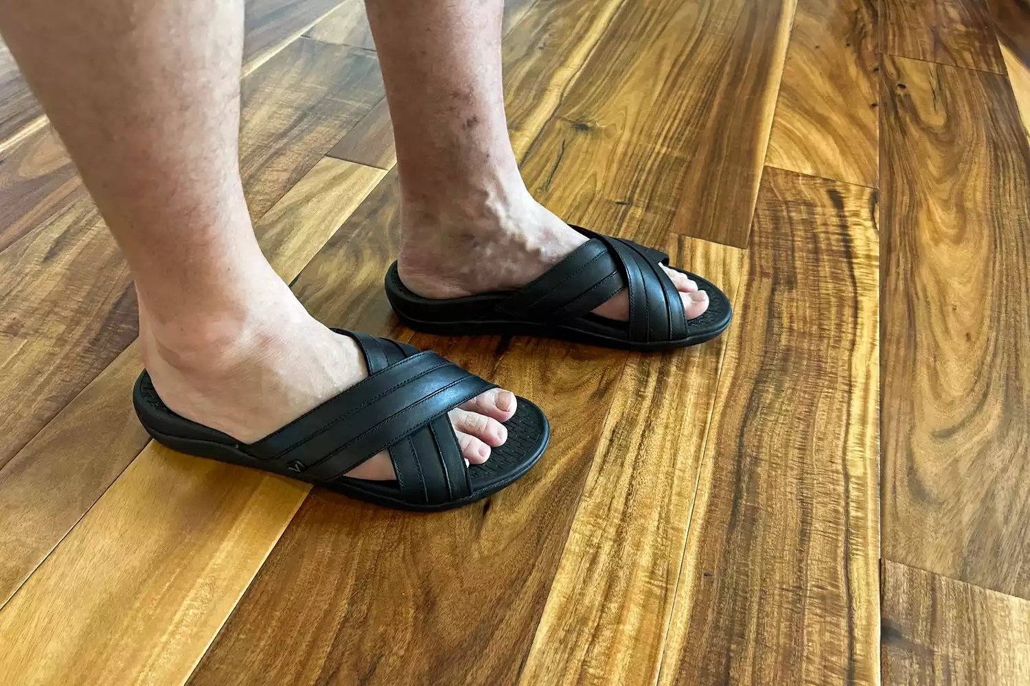 A person wears the Vionic Men's Tide Slide Sandals on a wooden floor