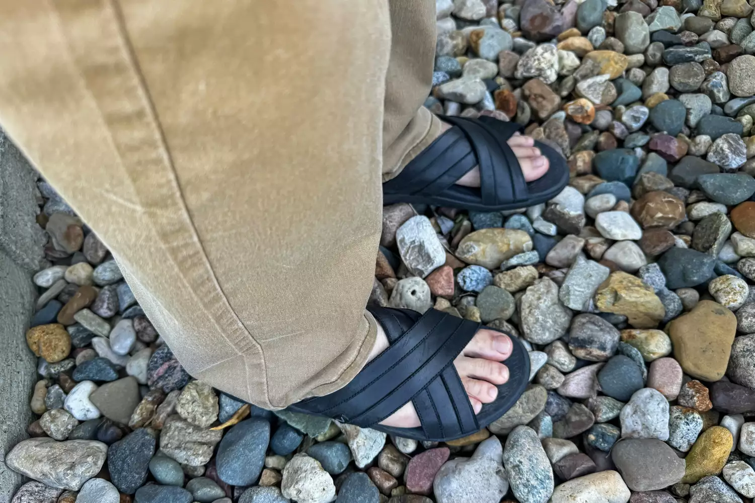 A person stands on pebbles while wearing the Vionic Men's Tide Slide Sandals