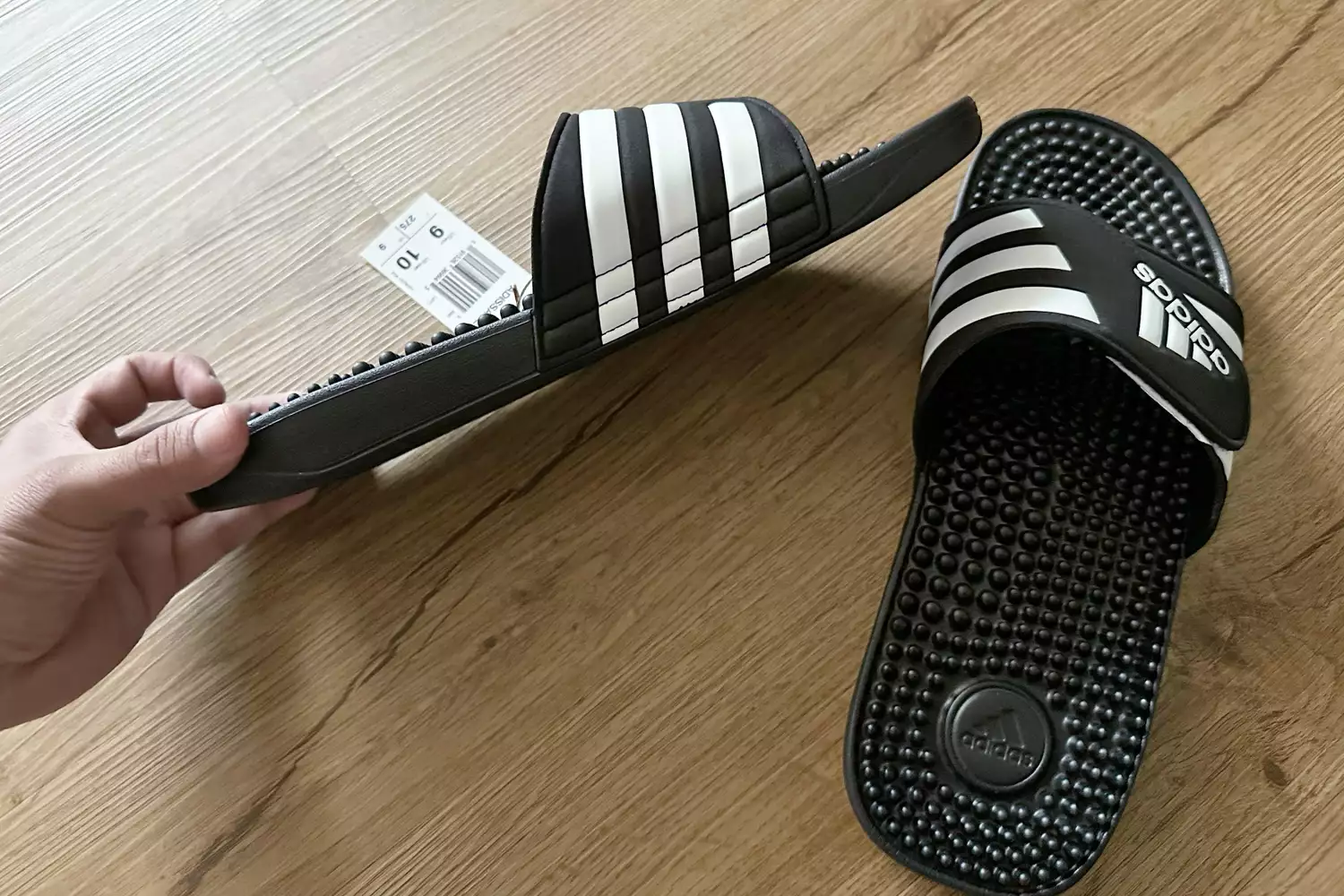 Hand holding Adidas Adissage Slides with tag on 