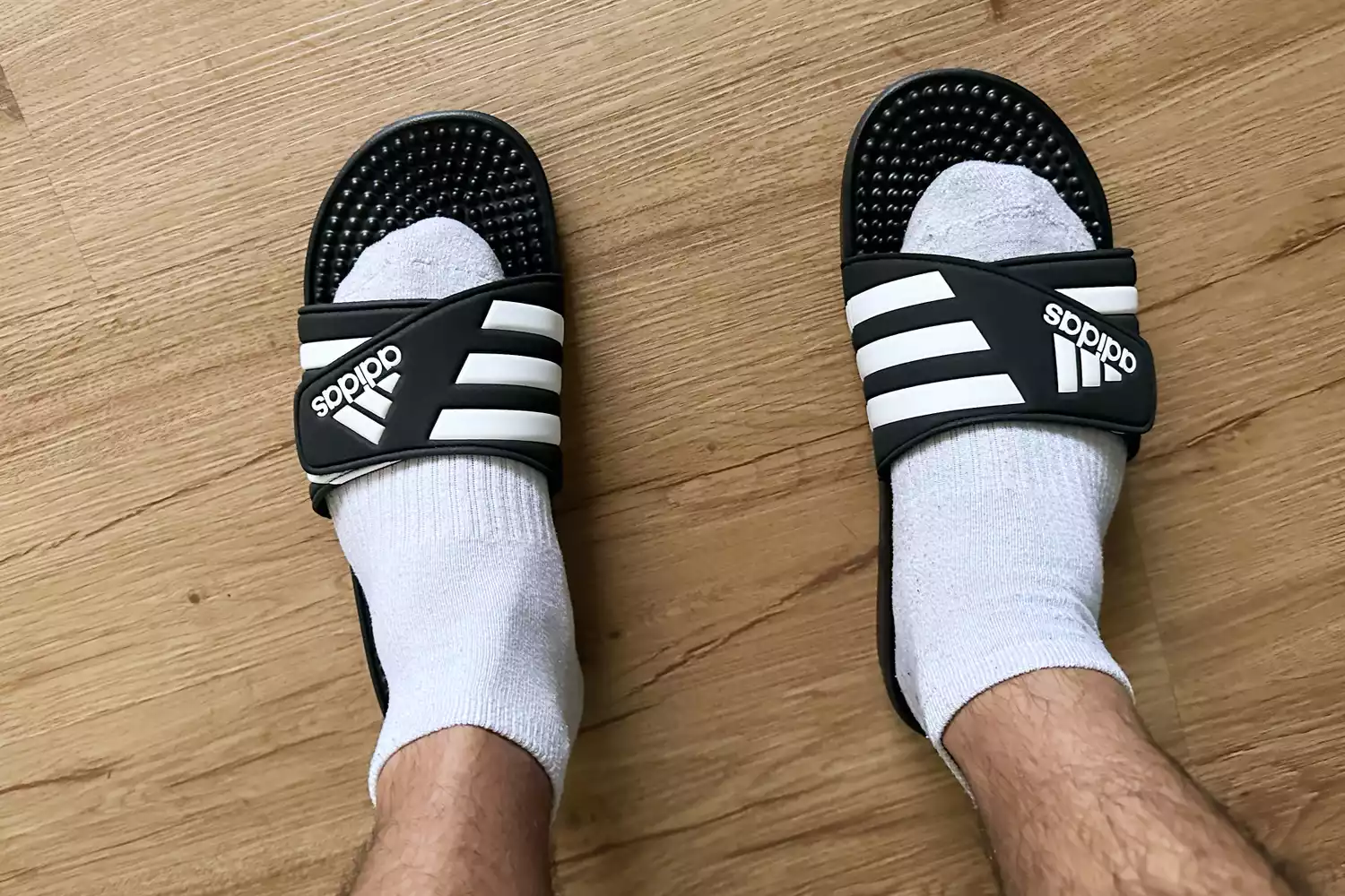 Person wearing Adidas Adissage Slides with socks on wood floor