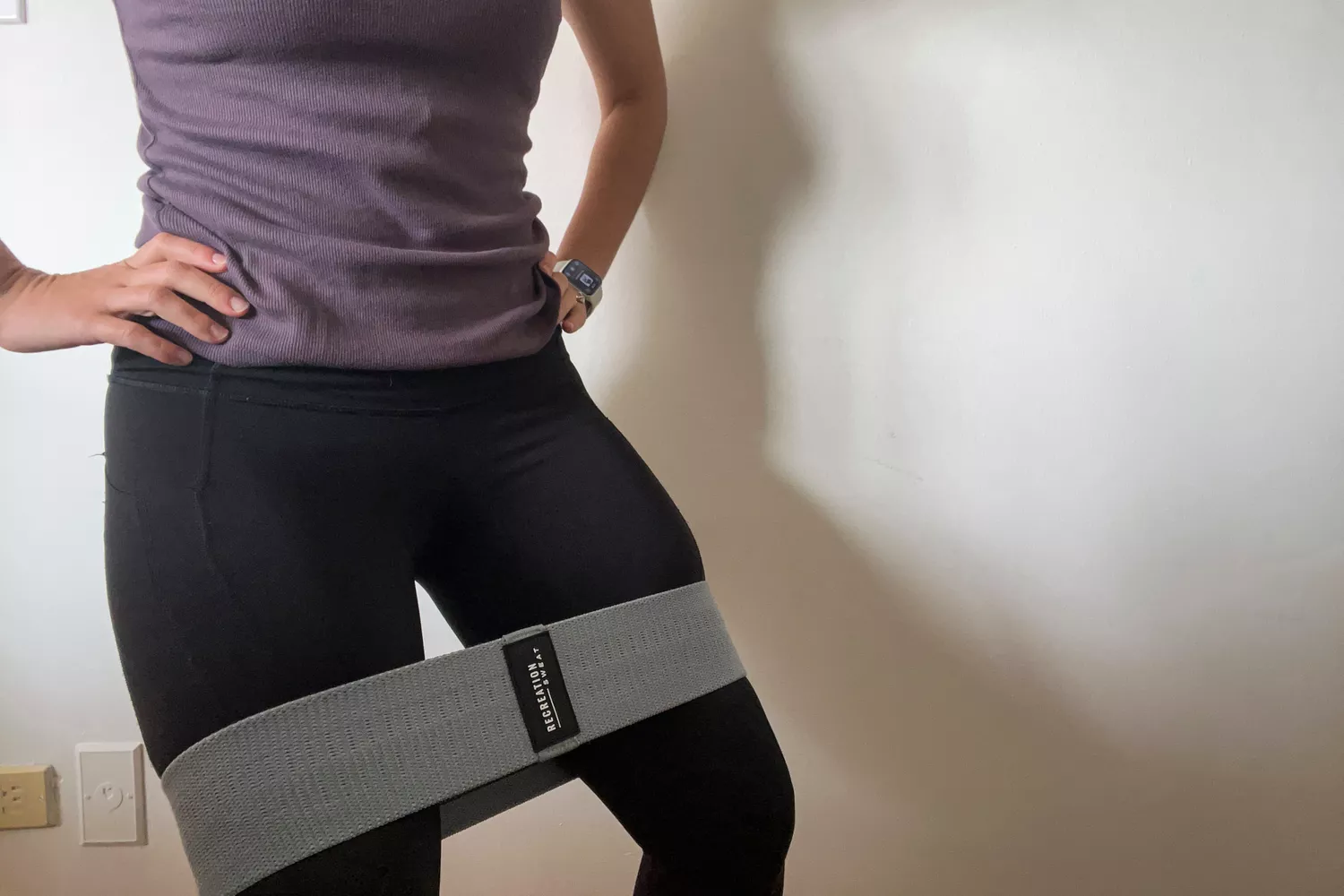 A close-up of a person in front of a white wall wearing a Recreation Sweat Resistance Band 2.0 around their thighs