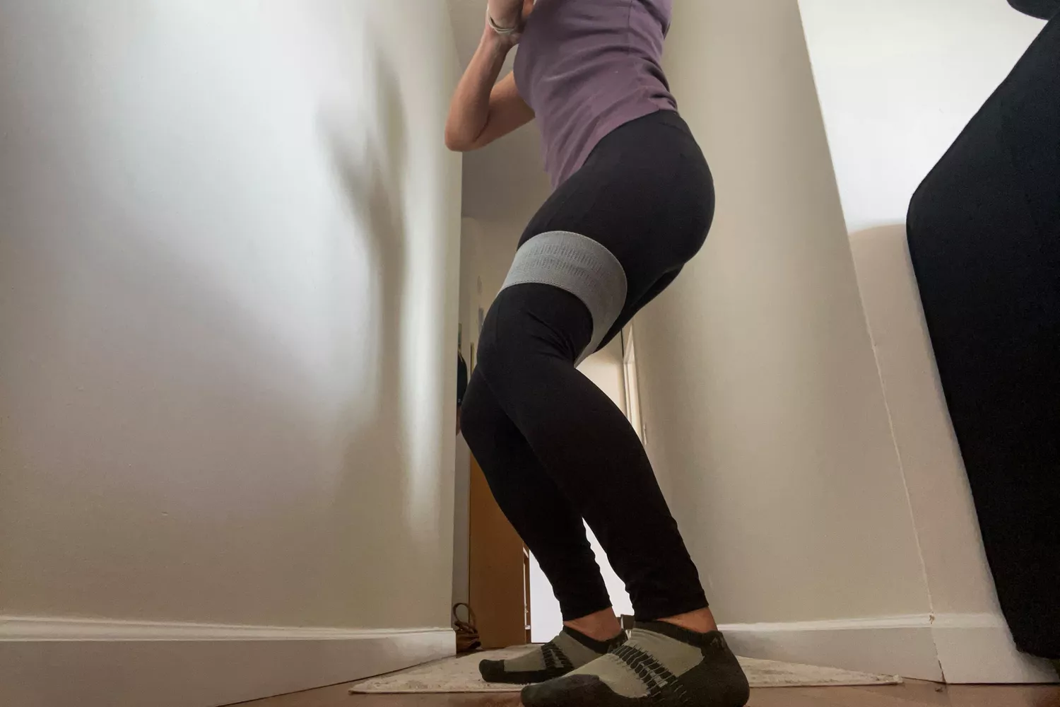 A person in a hallway exercising with the Recreation Sweat Resistance Band 2.0 around their thighs