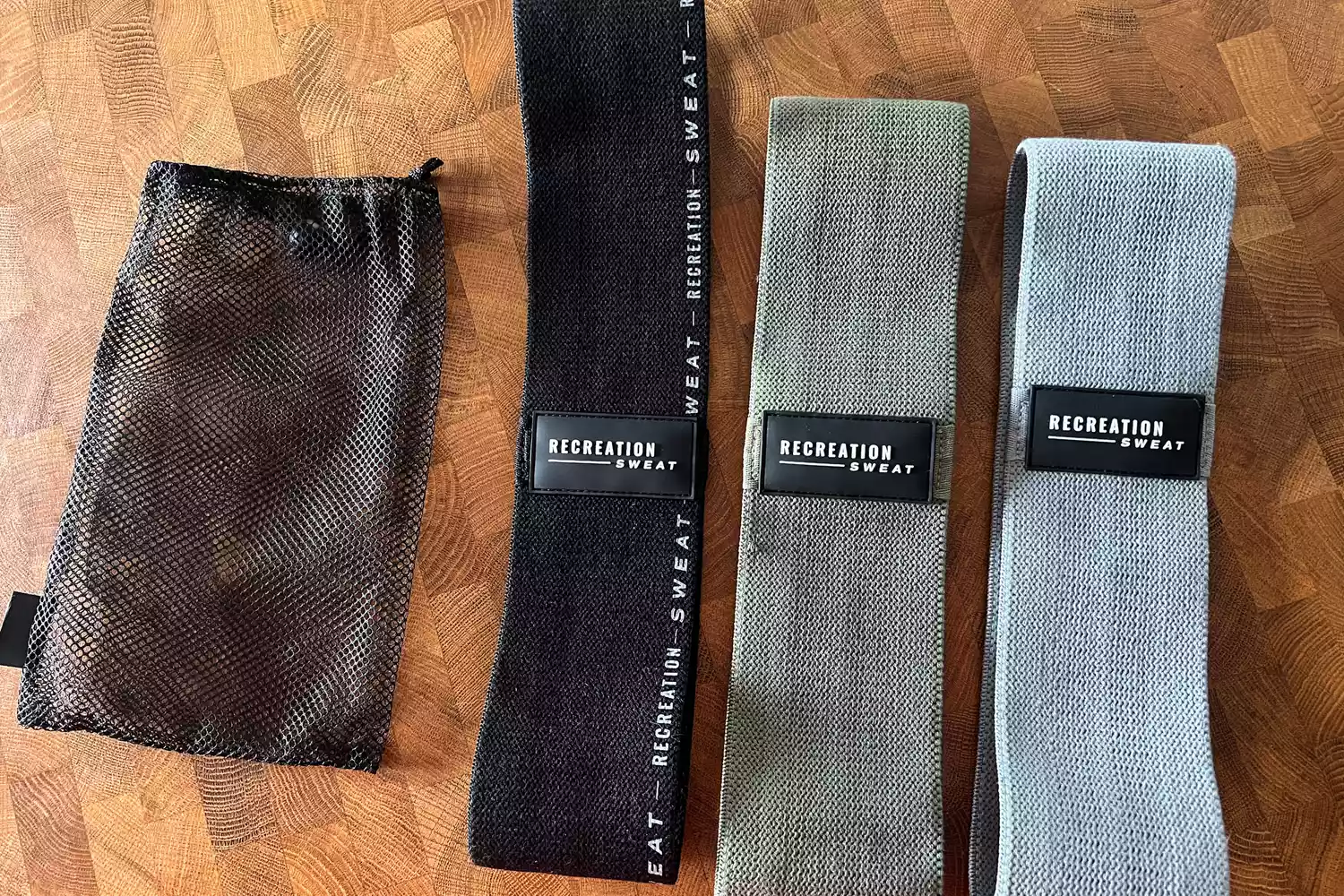 The Recreation Sweat Resistance Bands 2.0 lined up next to their mesh carrying case on a wooden surface