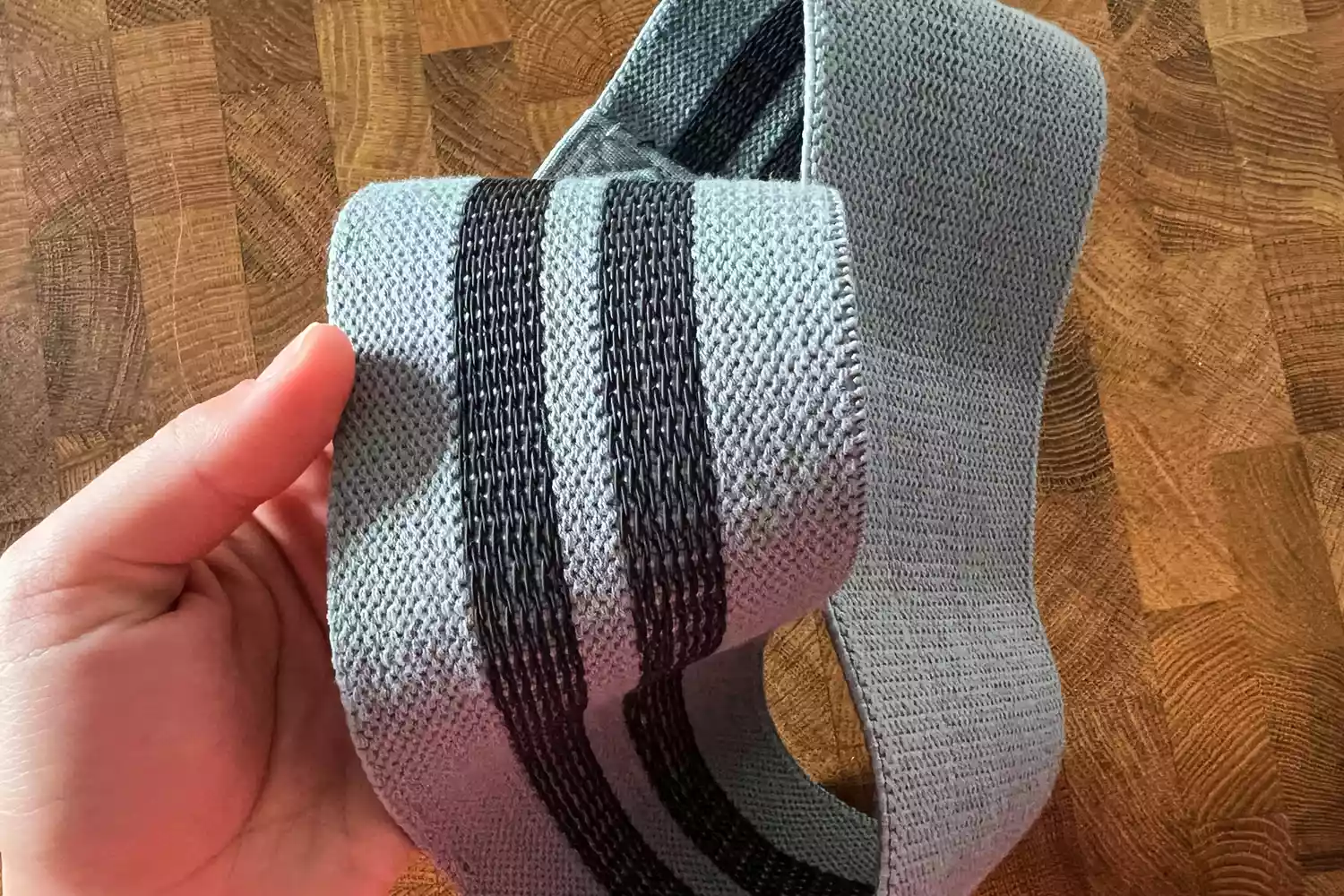 A hand holding a Recreation Sweat Resistance Band 2.0 over a wooden surface