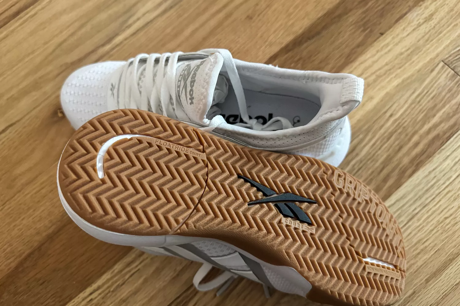 The Reebok Nano Court sneakers posed to show the bottom of a shoe on wood