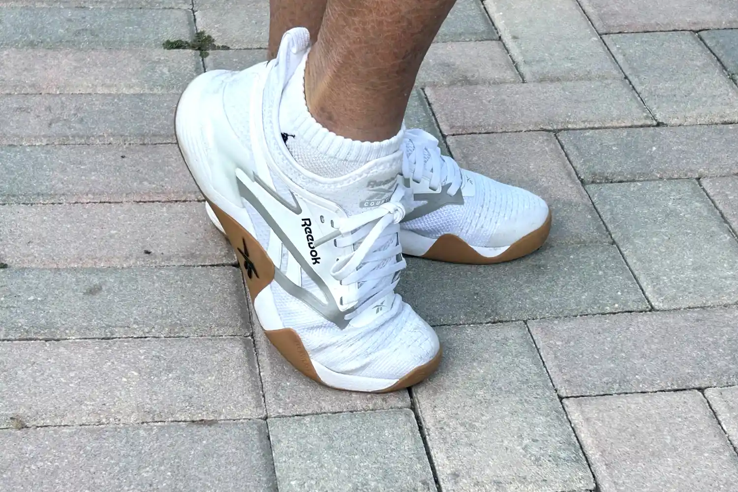 A person wears the Reebok Women's Nano Court Shoes on bricks