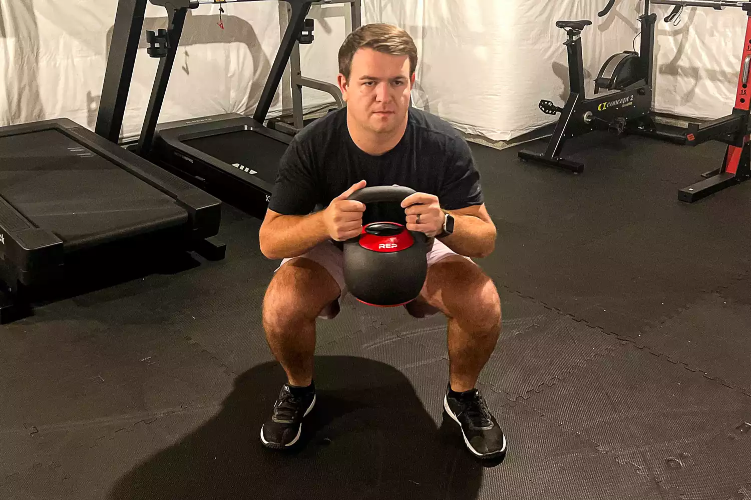 A person holds the REP Fitness Adjustable Kettlebell with Matte Powder Coating while squatting