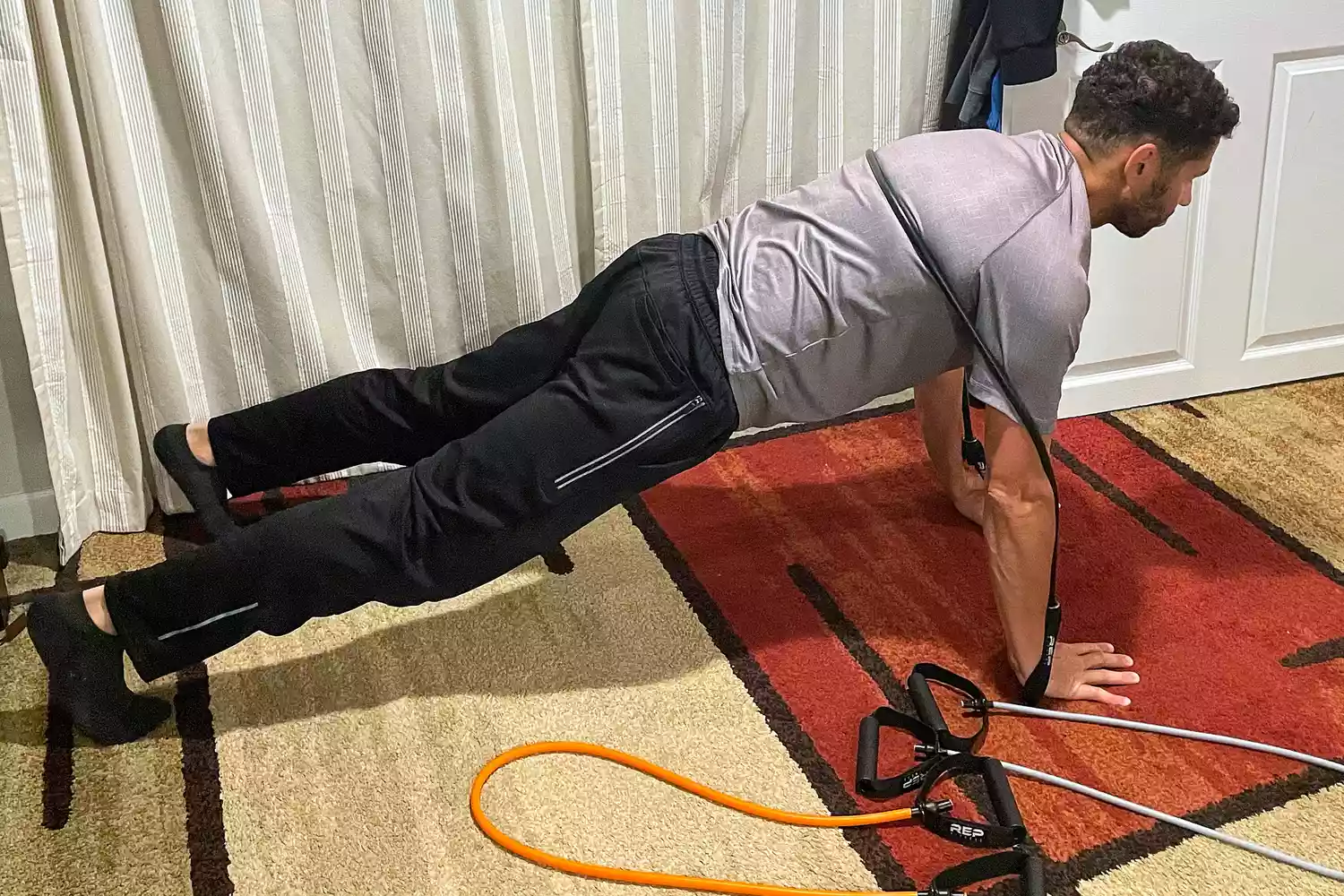 A person using the black Rep Fitness Tube Resistance Bands with Handles while doing pushups on a rugged floor