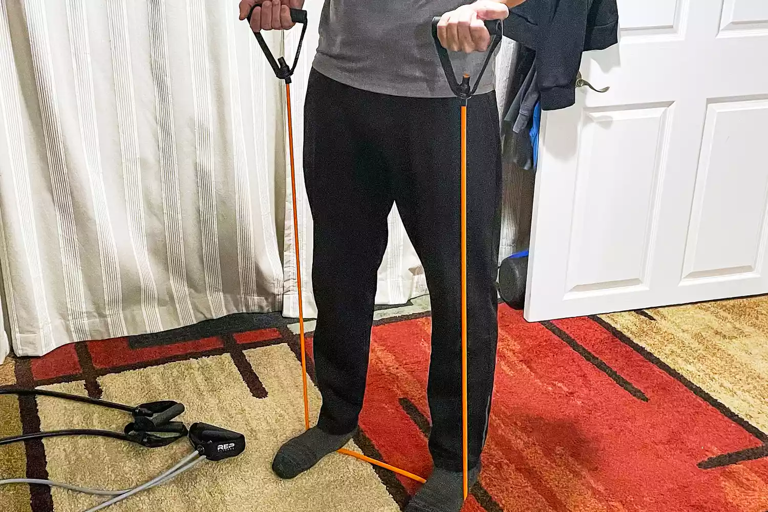 A person using the Rep Fitness Tube Resistance Bands with Handles while standing on a rug