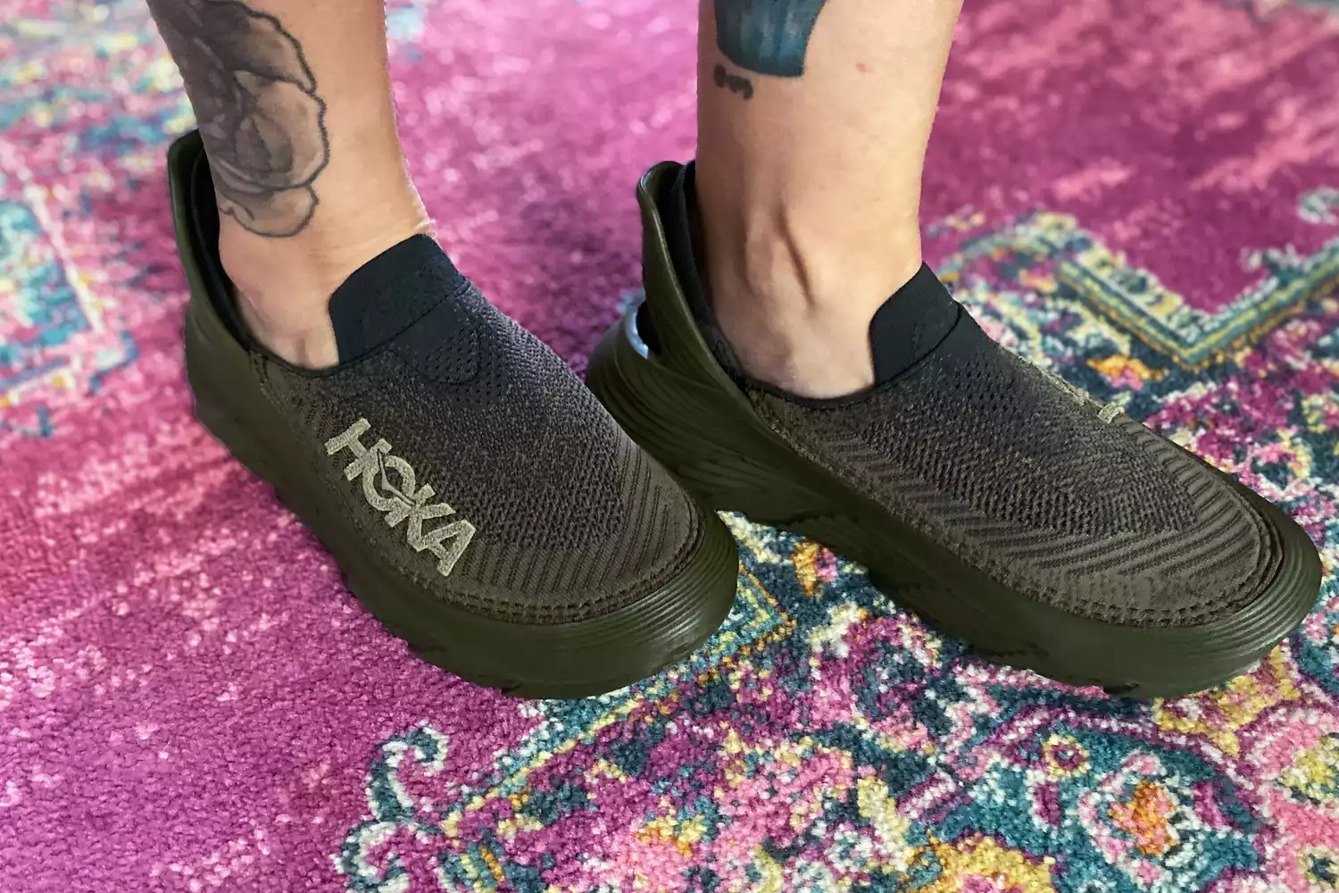 A person wearing Hoka Restore TC Recovery Shoes on a rug