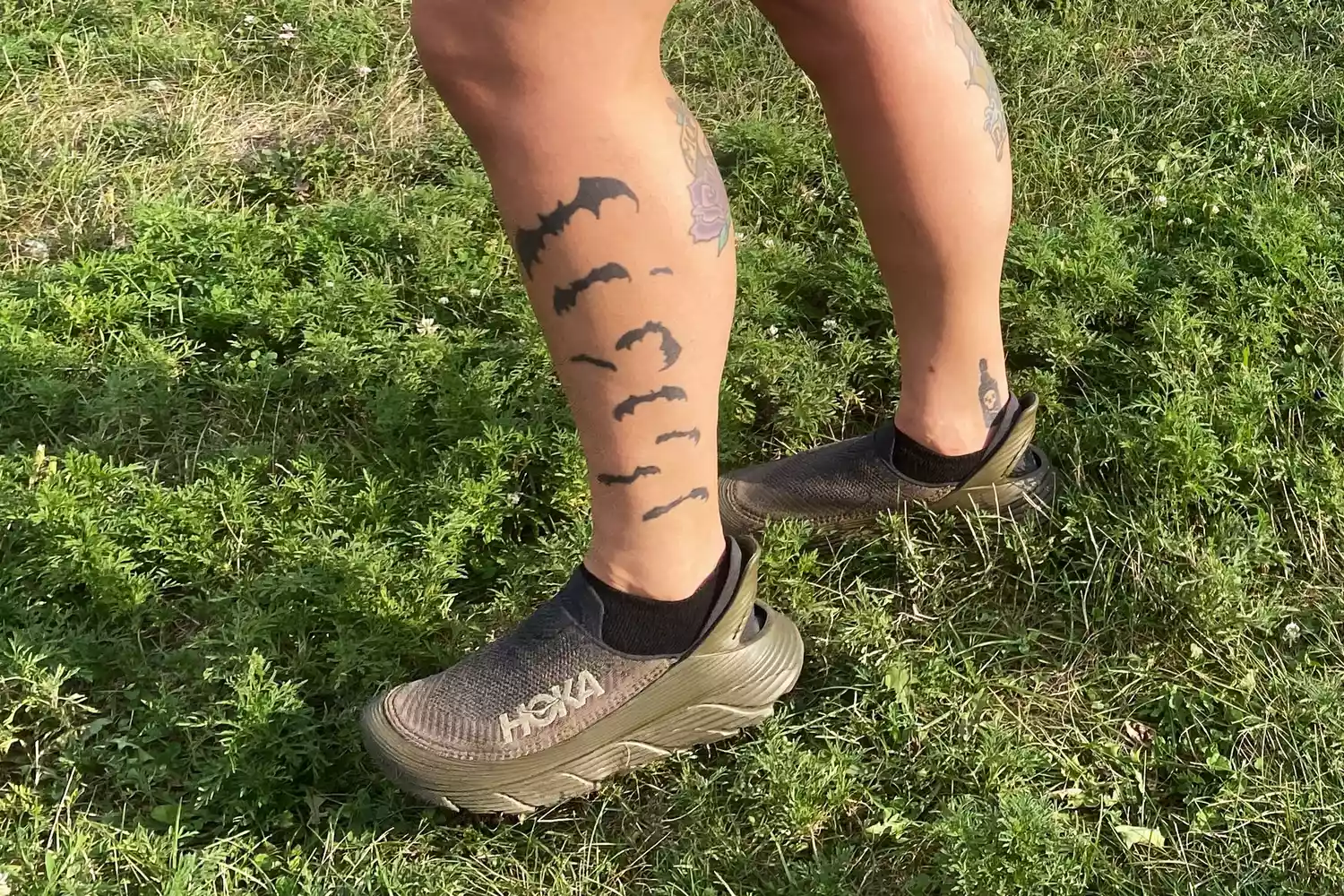 A person standing on grass while wearing the Hoka Restore TC Recovery Shoes