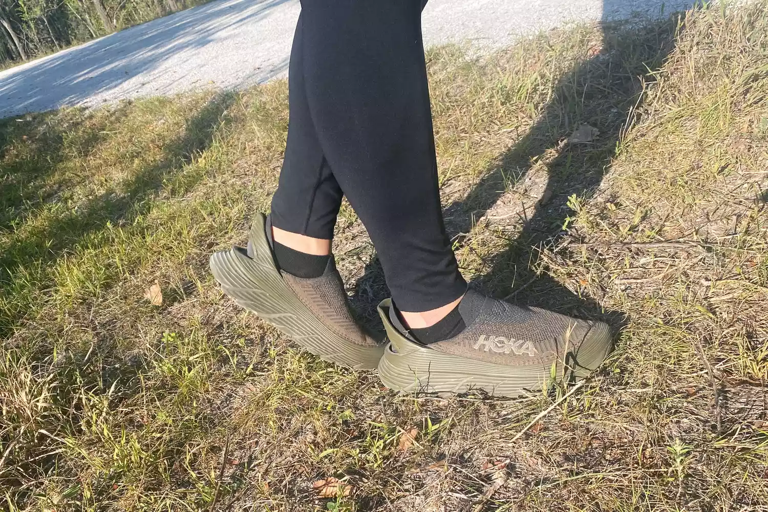 A person's legs posing while wearing Hoka Restore TC Recovery Shoes