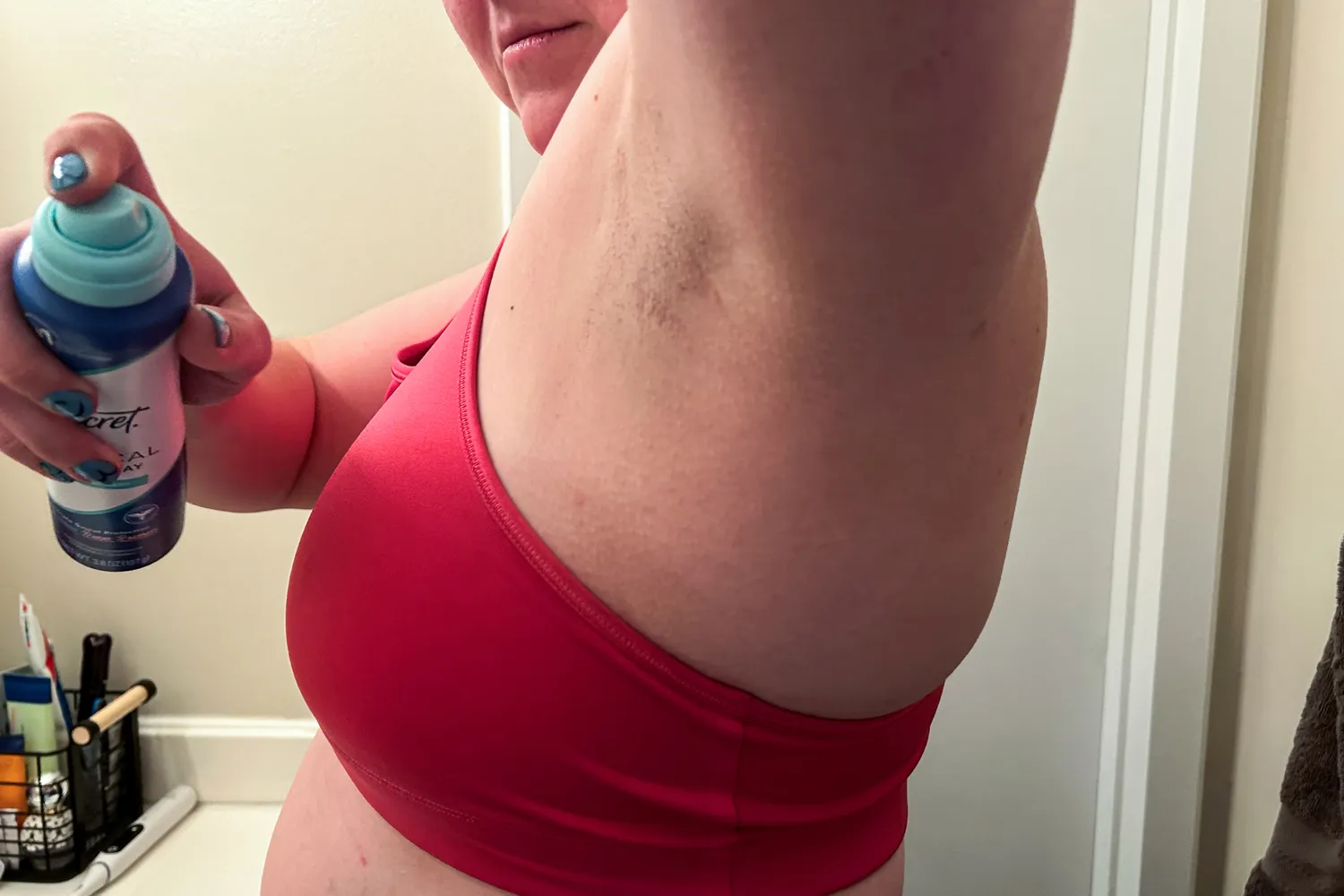 A person applies Secret Clinical Strength Dry Spray Antiperspirant Deodorant to their underarm