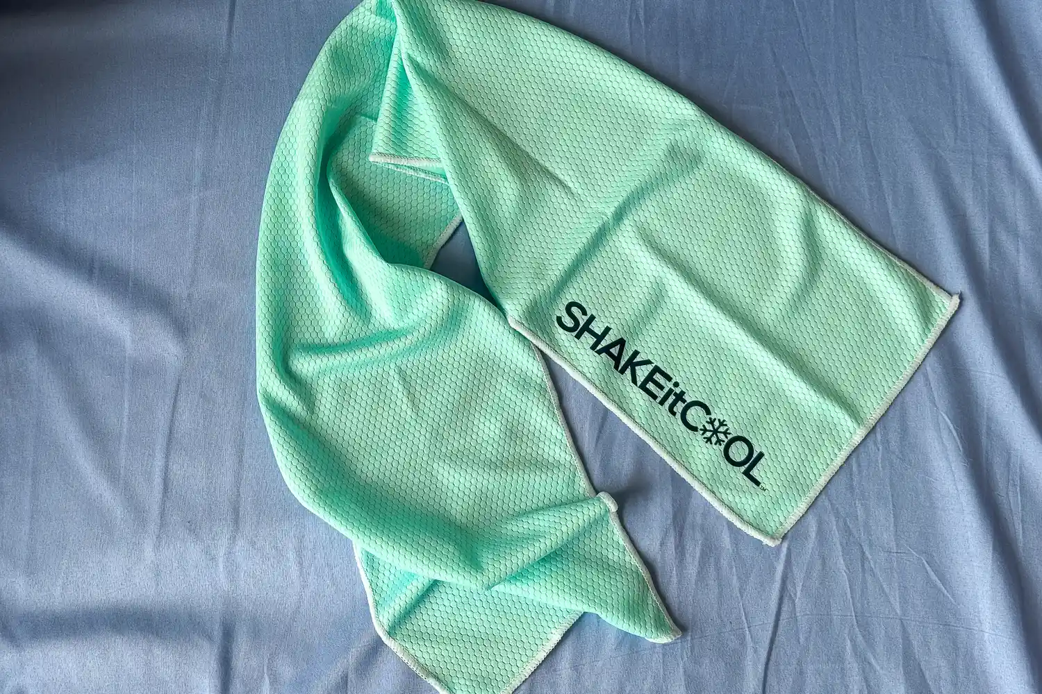 The SHAKEitCOOL Original Cooling Towel on a blue sheet