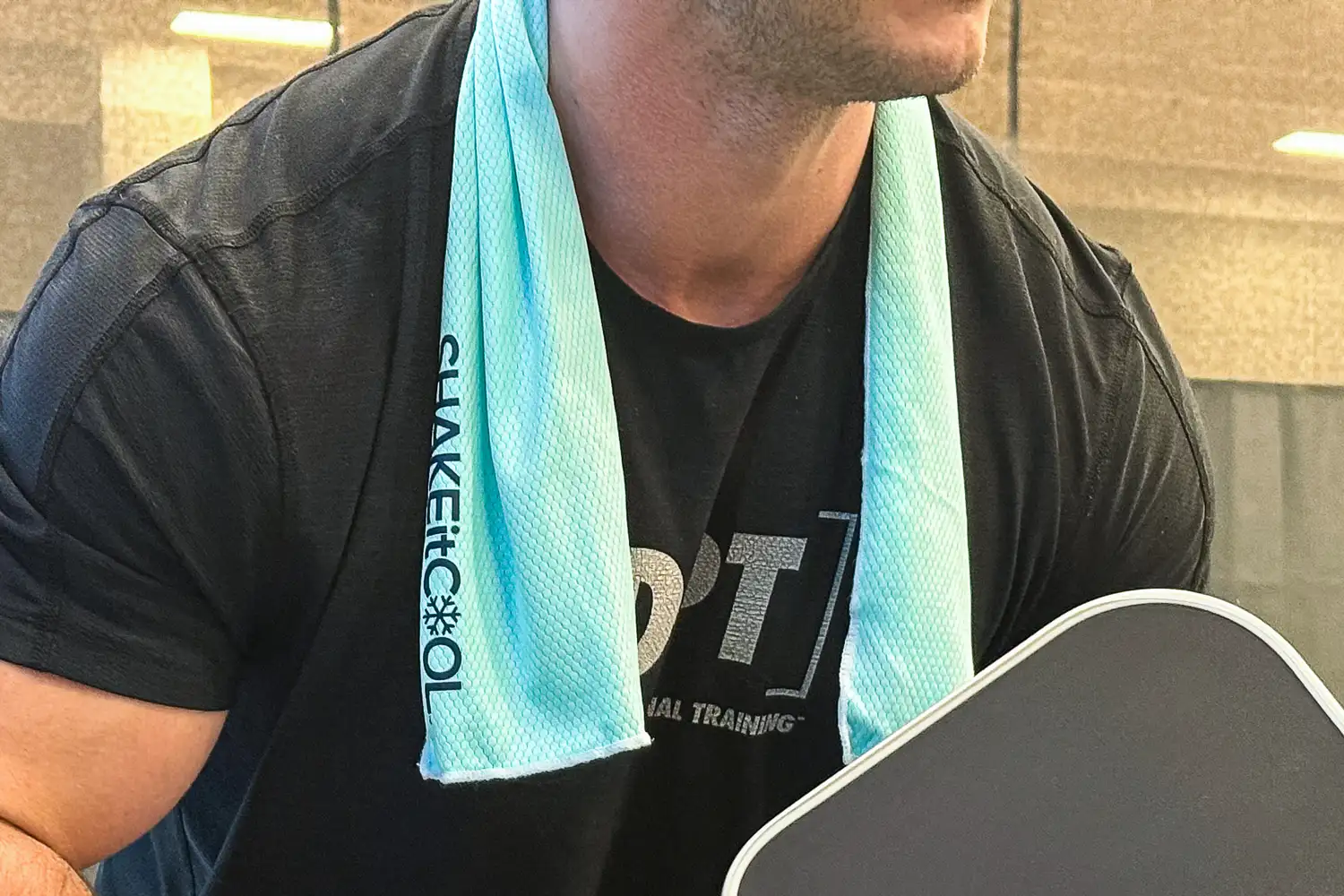 A person plays paddleball with the SHAKEitCOOL Original Cooling Towel around their neck