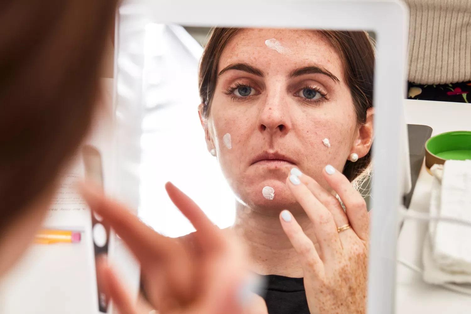 Reflection of a person applying moisturizer to their face