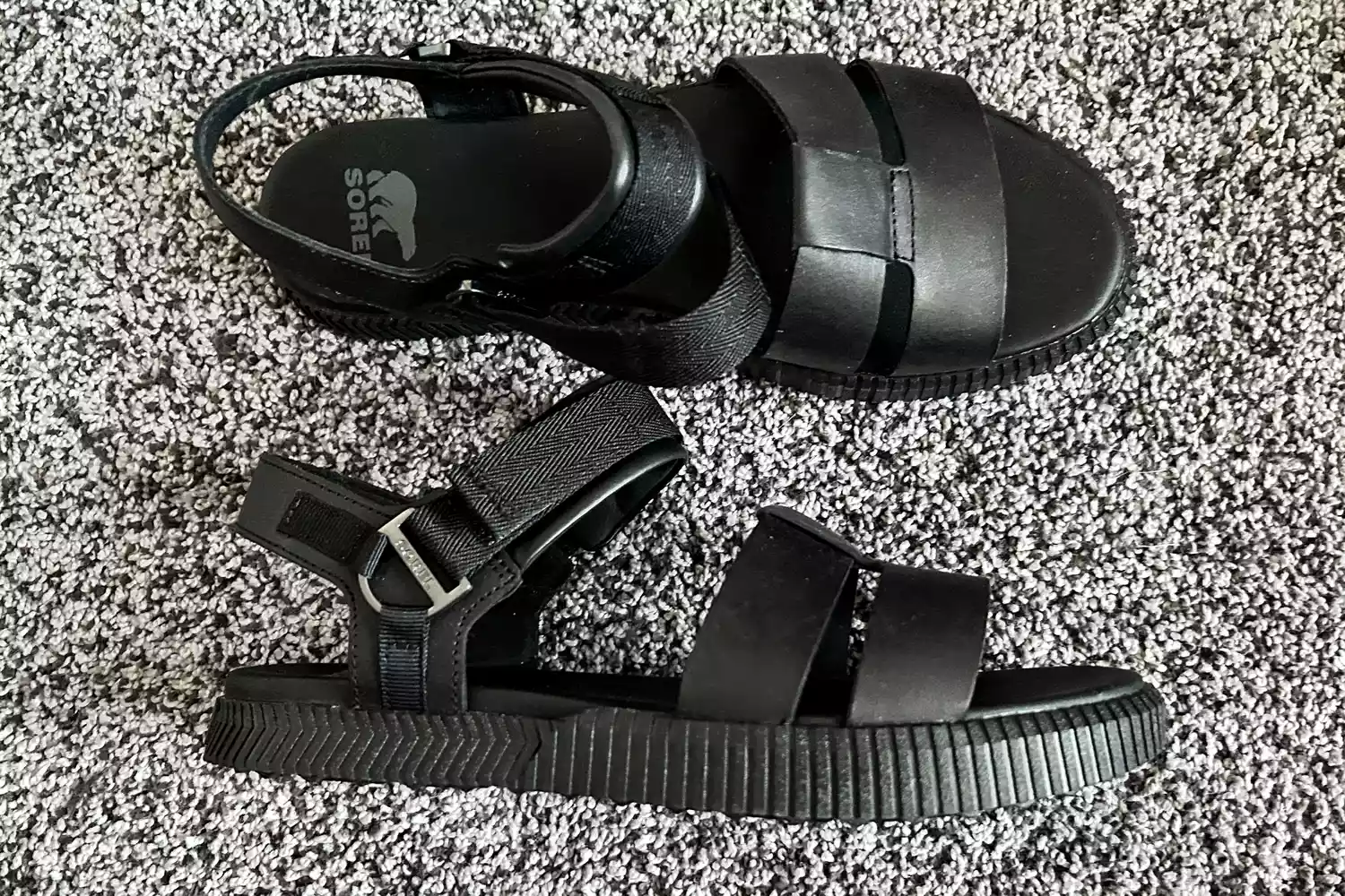 The Sorel ONA AVE Women's Ankle Strap Flat Sandals posed on carpet