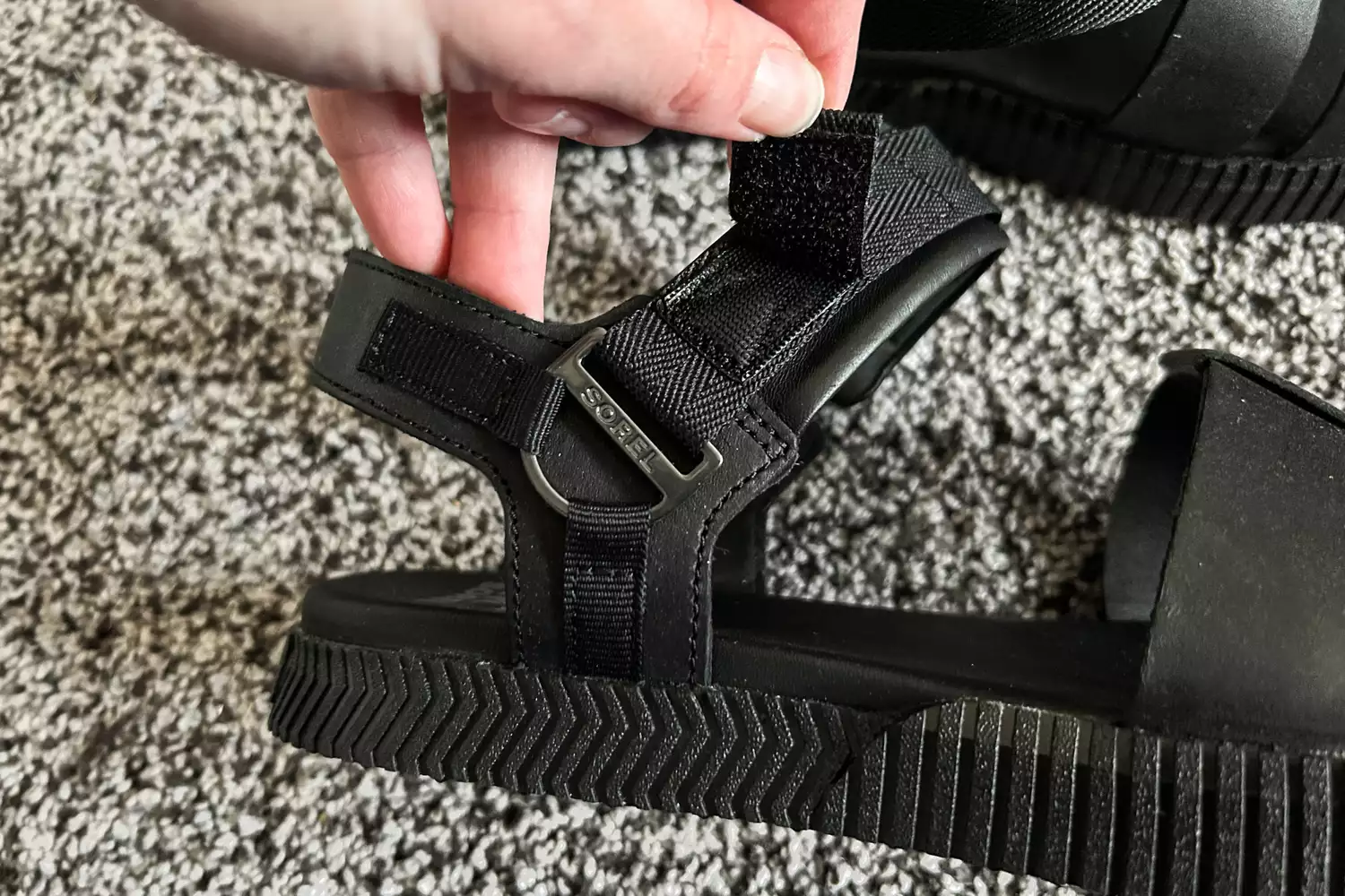 A hand showing the straps on the Sorel ONA AVE Women's Ankle Strap Flat Sandal